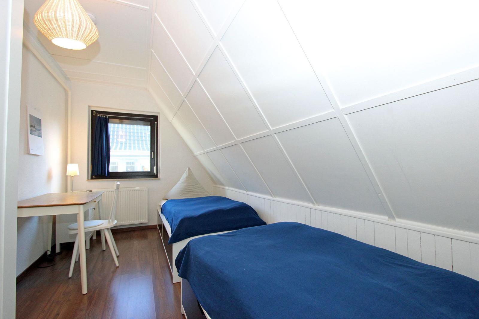 Zimmer mit zwei Betten, Schreibtisch und Fenster. Dachschrägen Decke und Holzboden.