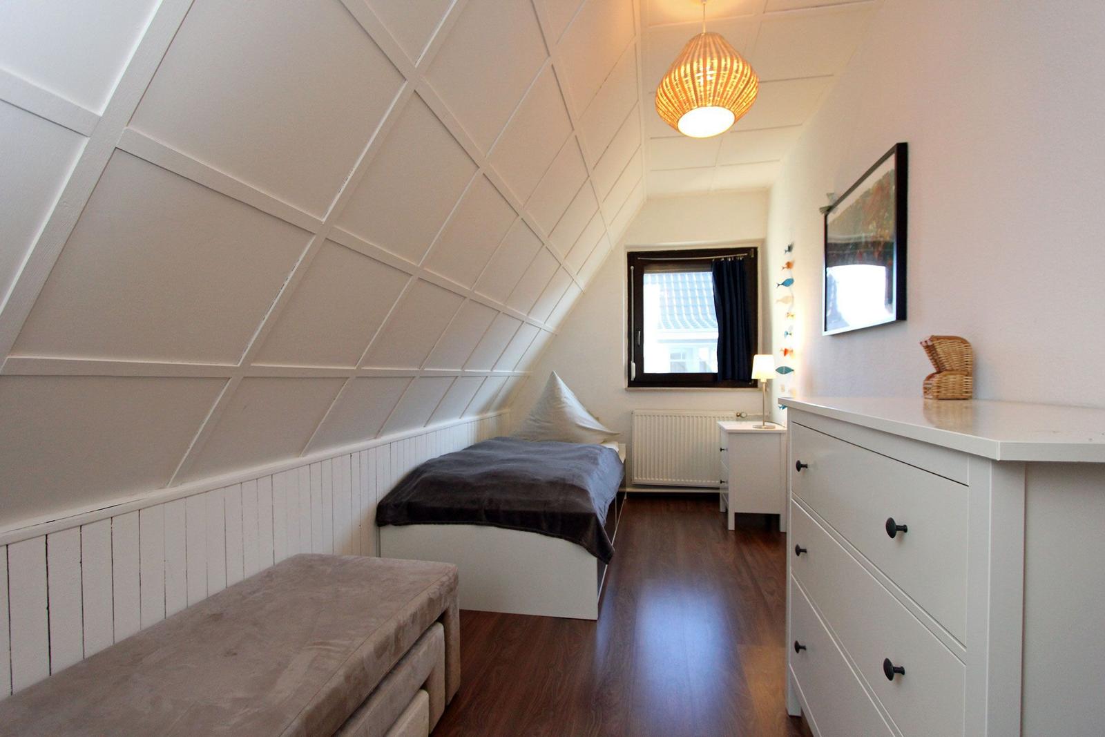 Schlafzimmer mit Dachschrägen, Bett, Schrank und Fenster.