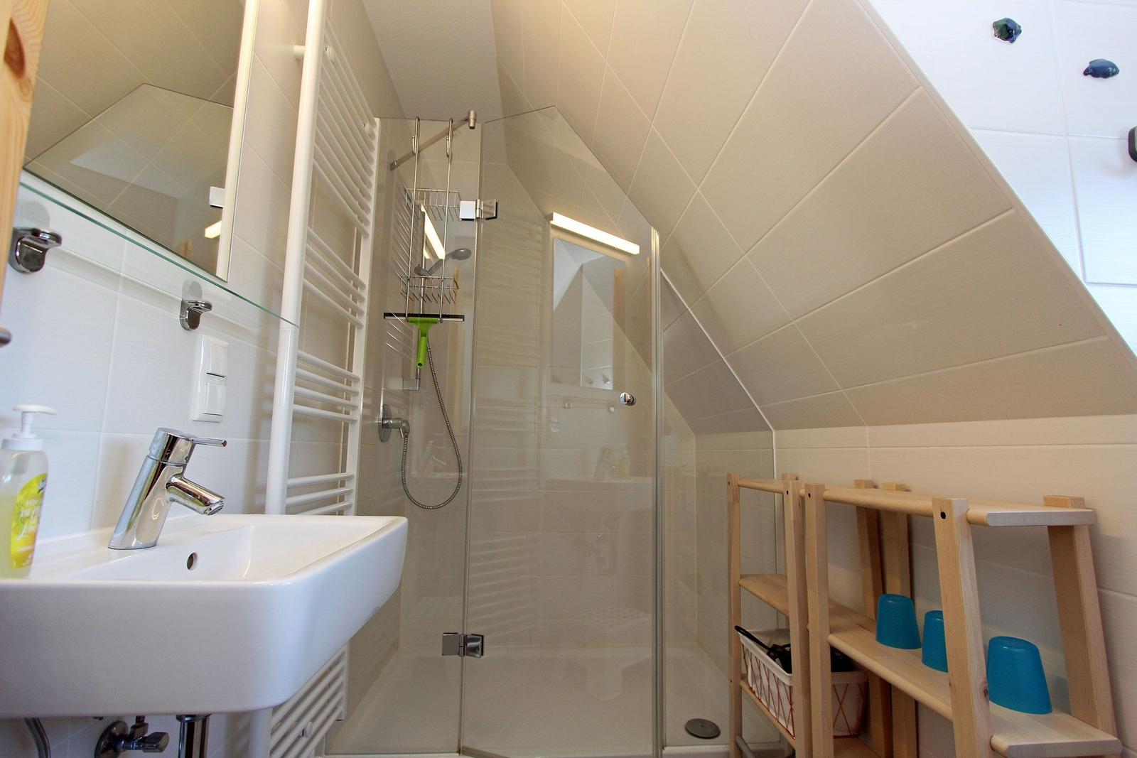 Badezimmer mit Dusche, Waschbecken und Holzregal