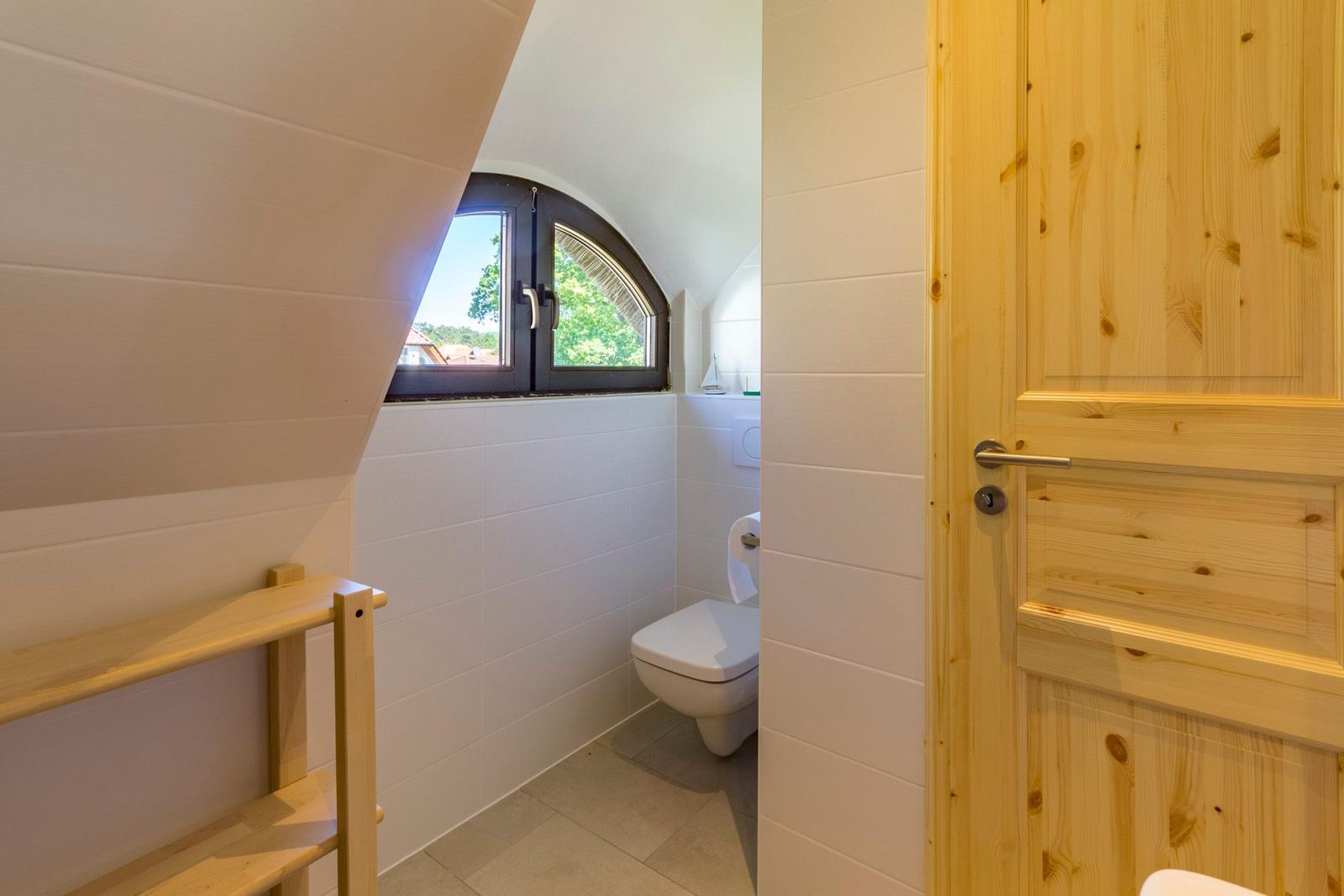 Bad mit Toilette und Holztür. Bogenfenster mit Blick nach draußen.
