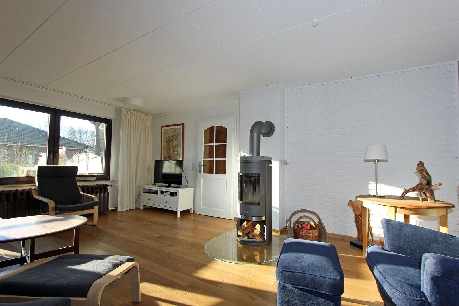 Wohnzimmer mit Holzofen, Fernseher und Sitzgelegenheiten.