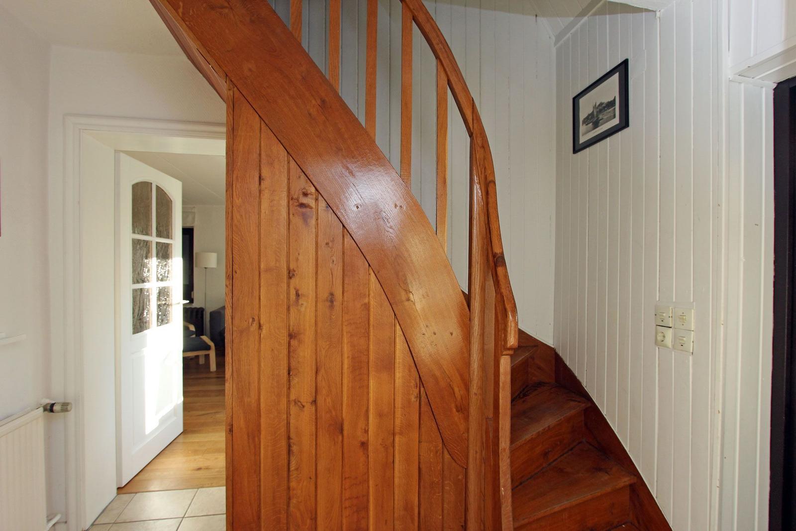 Holzgetreppe mit Geländer führt nach oben. Weiße Wände und Tür im Hintergrund.