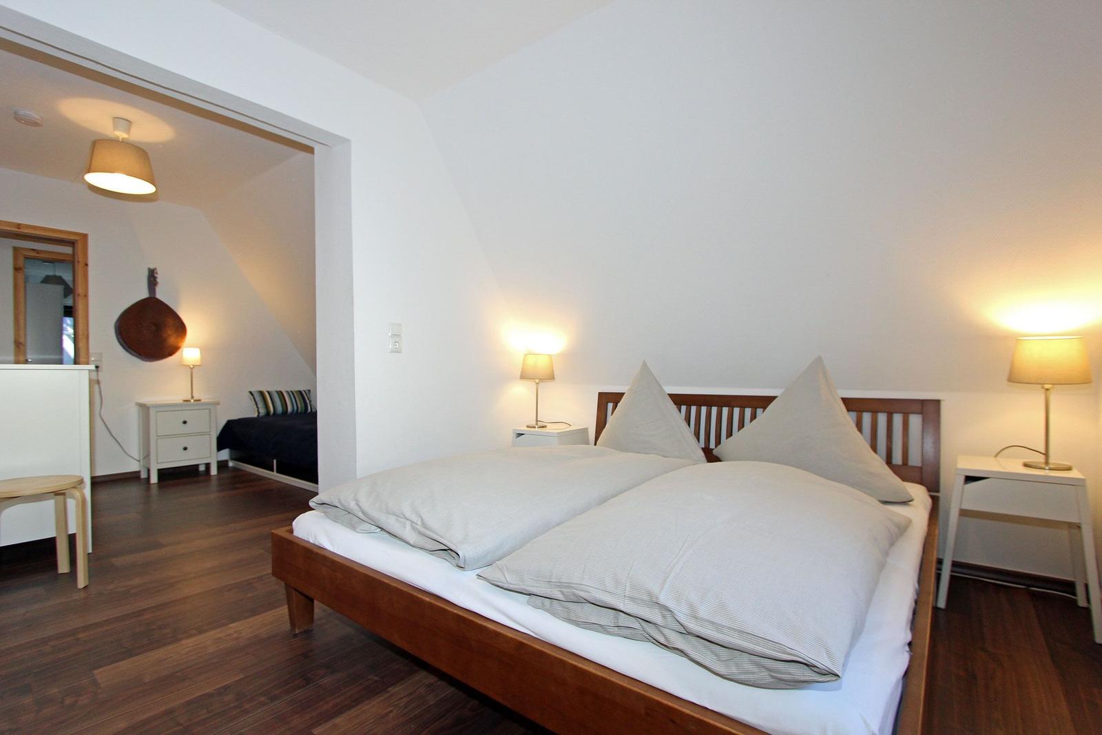 Schlafzimmer mit Doppelbett, Nachttischen und Lampen. Durchgang zum angrenzenden Raum.