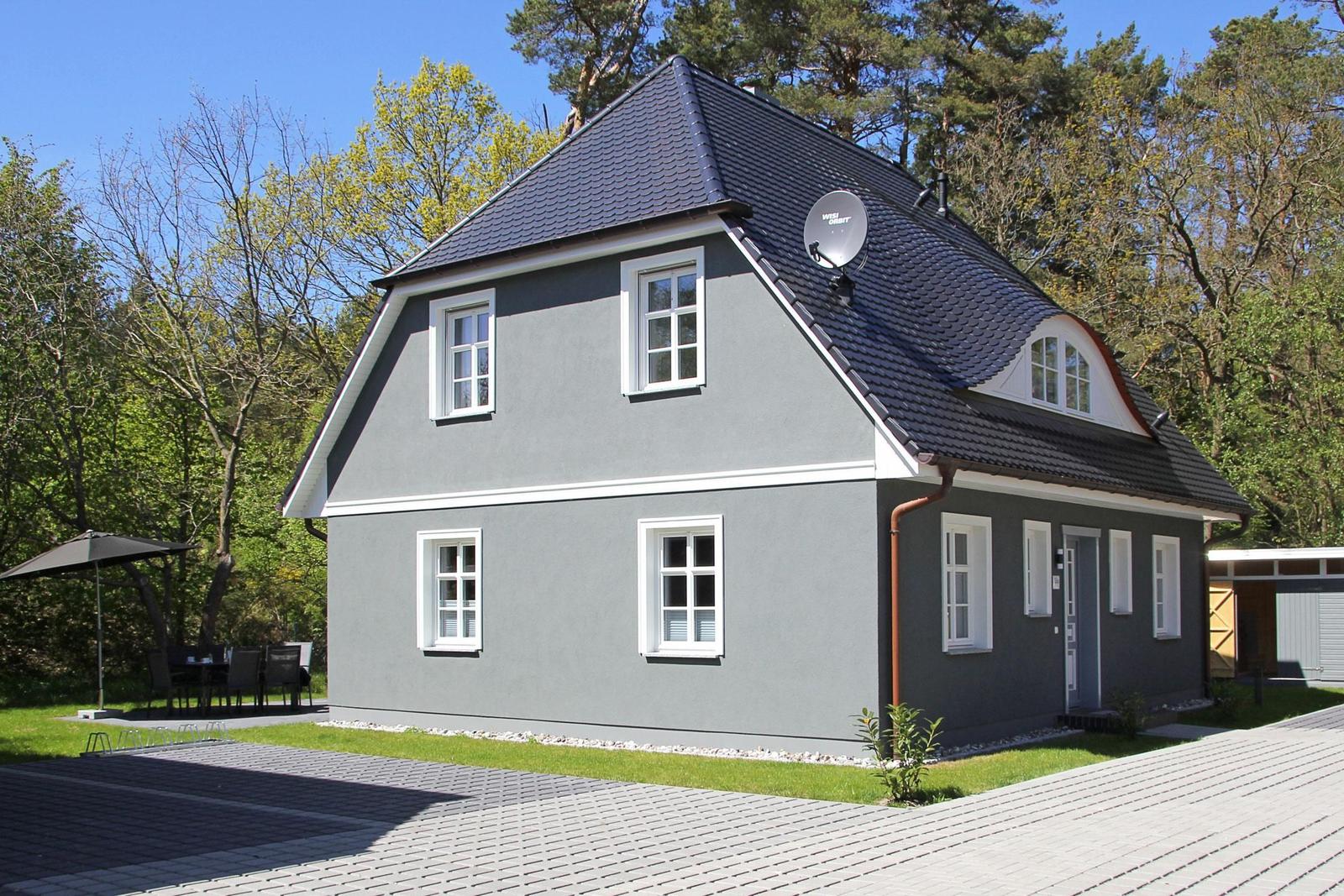 Ein graues Haus mit weißen Fenstern und einem dunklen Dach steht inmitten von Bäumen.