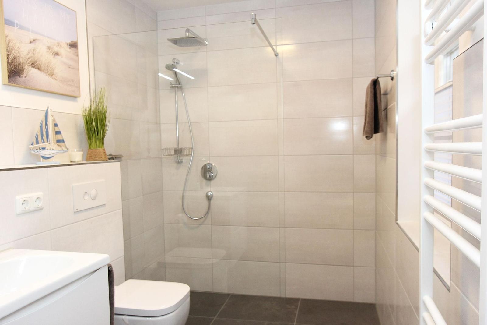 Badezimmer mit Dusche, Toilette und Waschbecken. Wandbild und Dekoobjekte sichtbar.