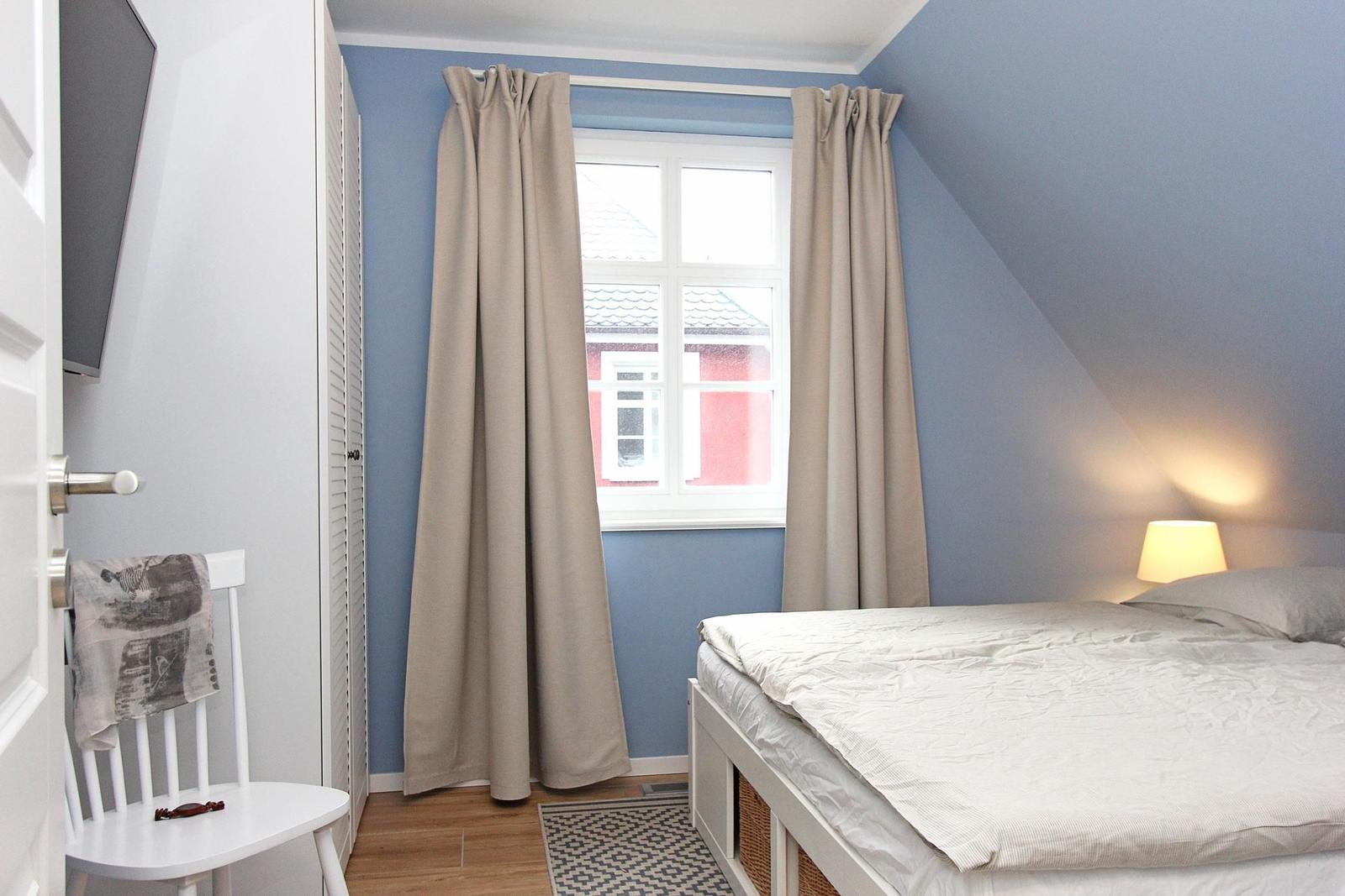 Schlafzimmer mit Bett, Fenster, Vorhängen und Lampen.