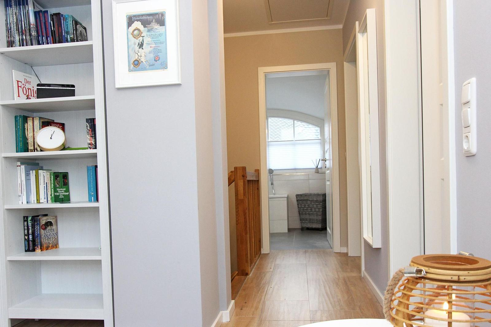 Flur mit Bücherregal, Treppe und Blick in die Küche.