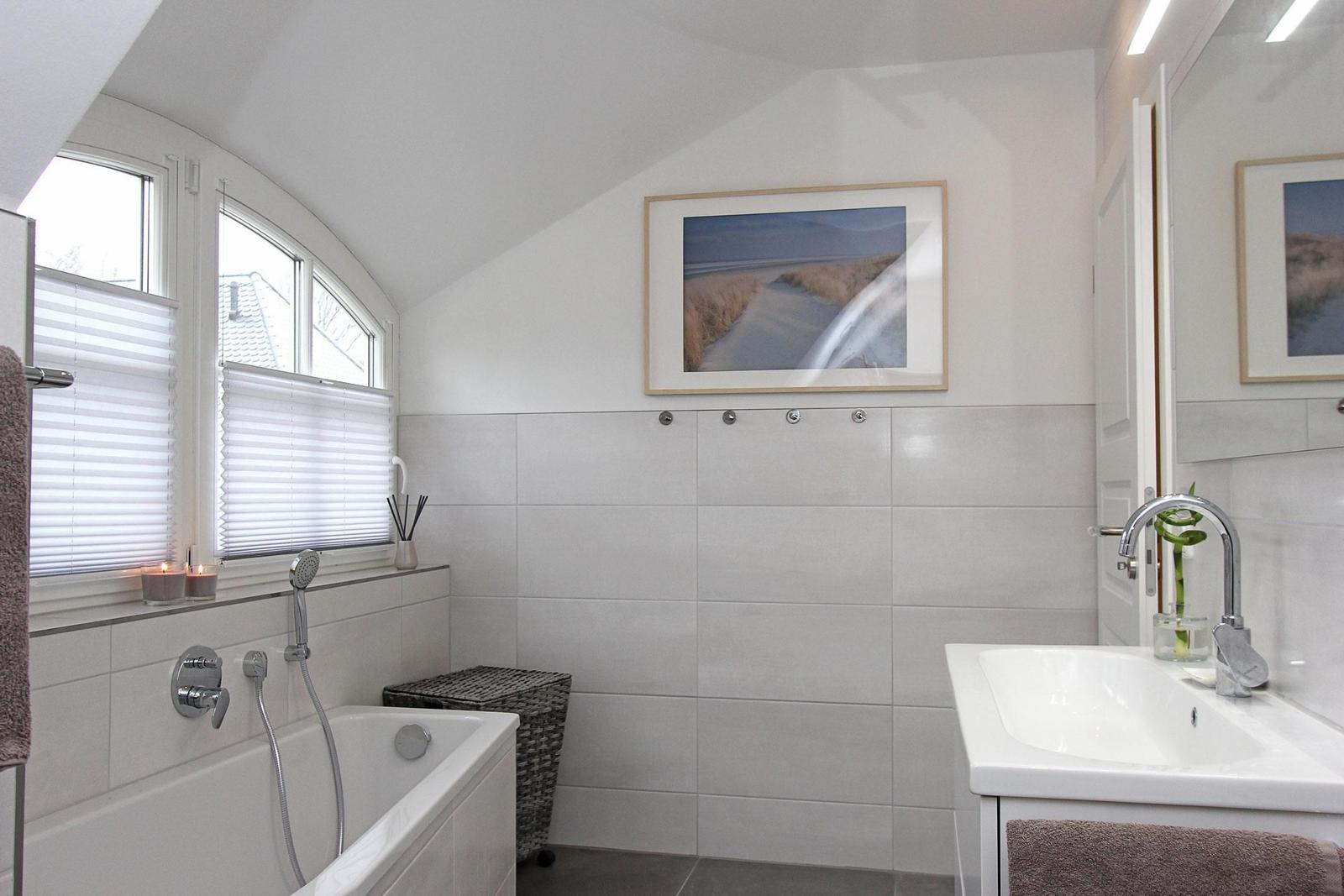 Badezimmer mit Badewanne, Waschbecken und Fenster mit Jalousien.