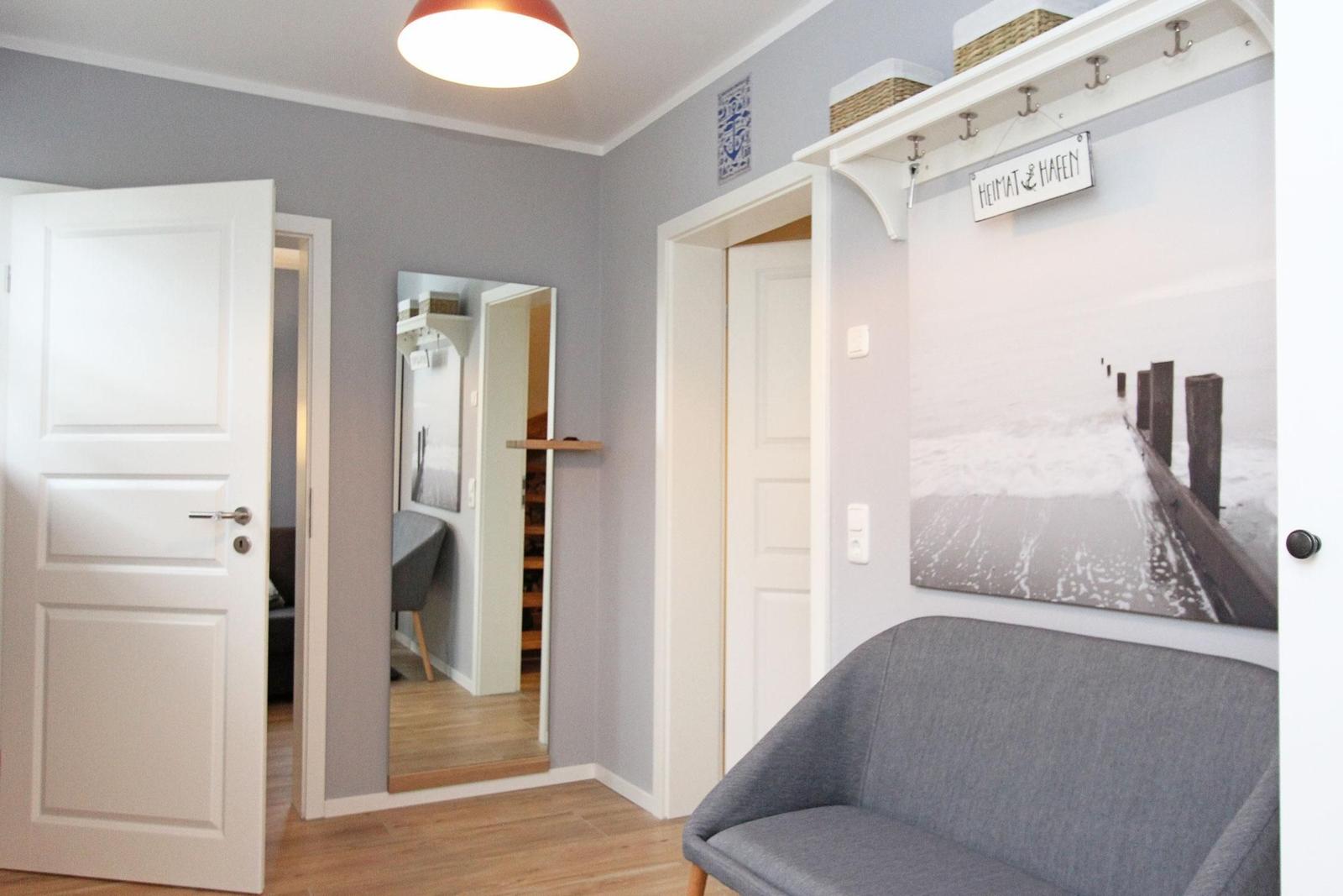 Eingangsbereich mit grauer Couch, Wandbild und Kleiderhaken. Durchgänge zu weiteren Räumen.