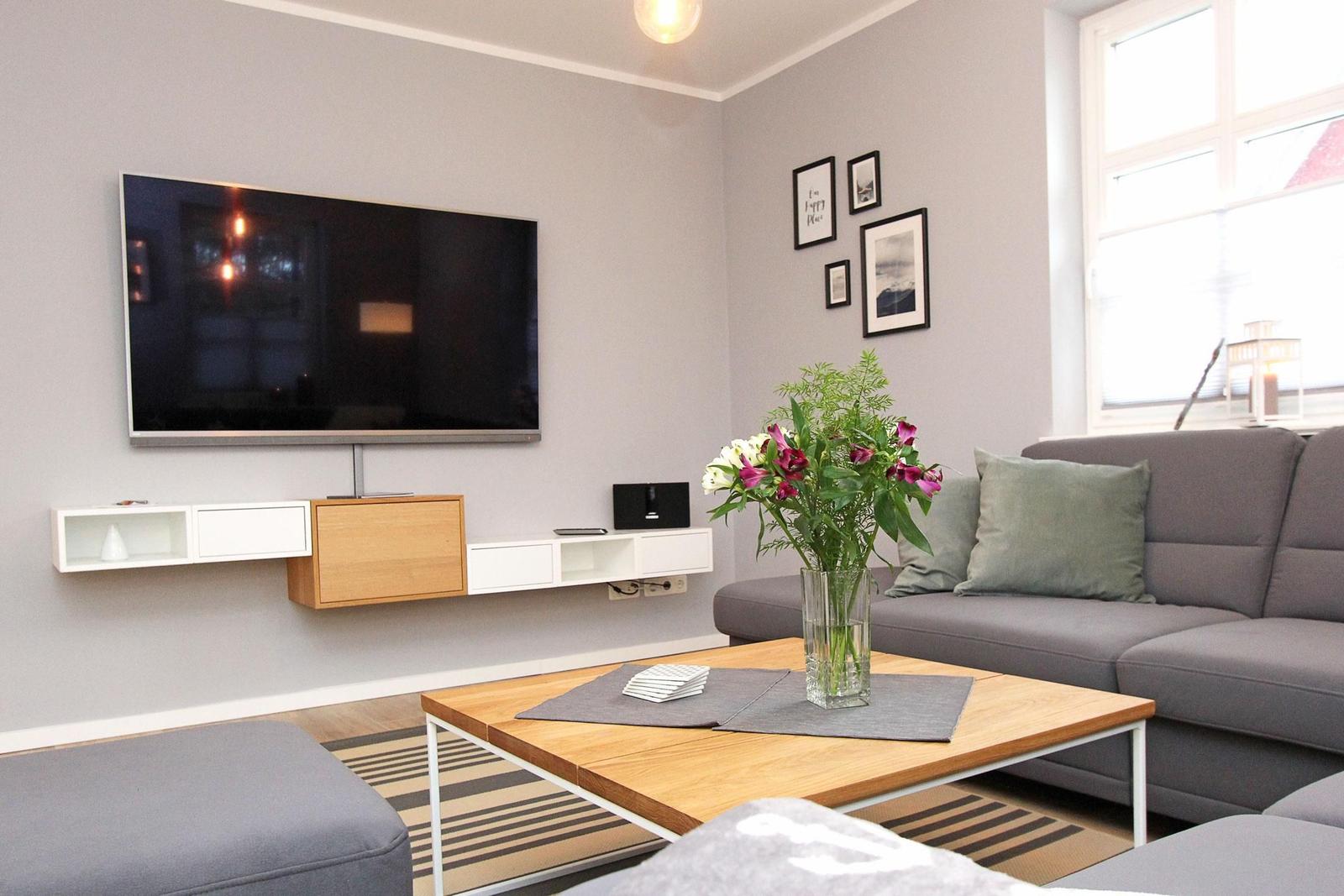 Wohnzimmer mit grauem Sofa, Holztisch und Wand-TV.
