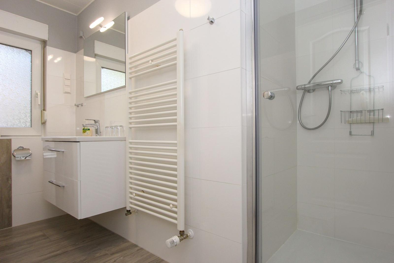 Badezimmer mit Dusche, Waschbecken und Heizkörper