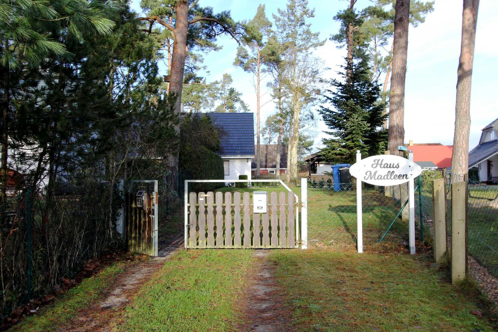 Haus Madleen mit Eingangstor und Schild. Umgeben von Bäumen und Grünfläche.