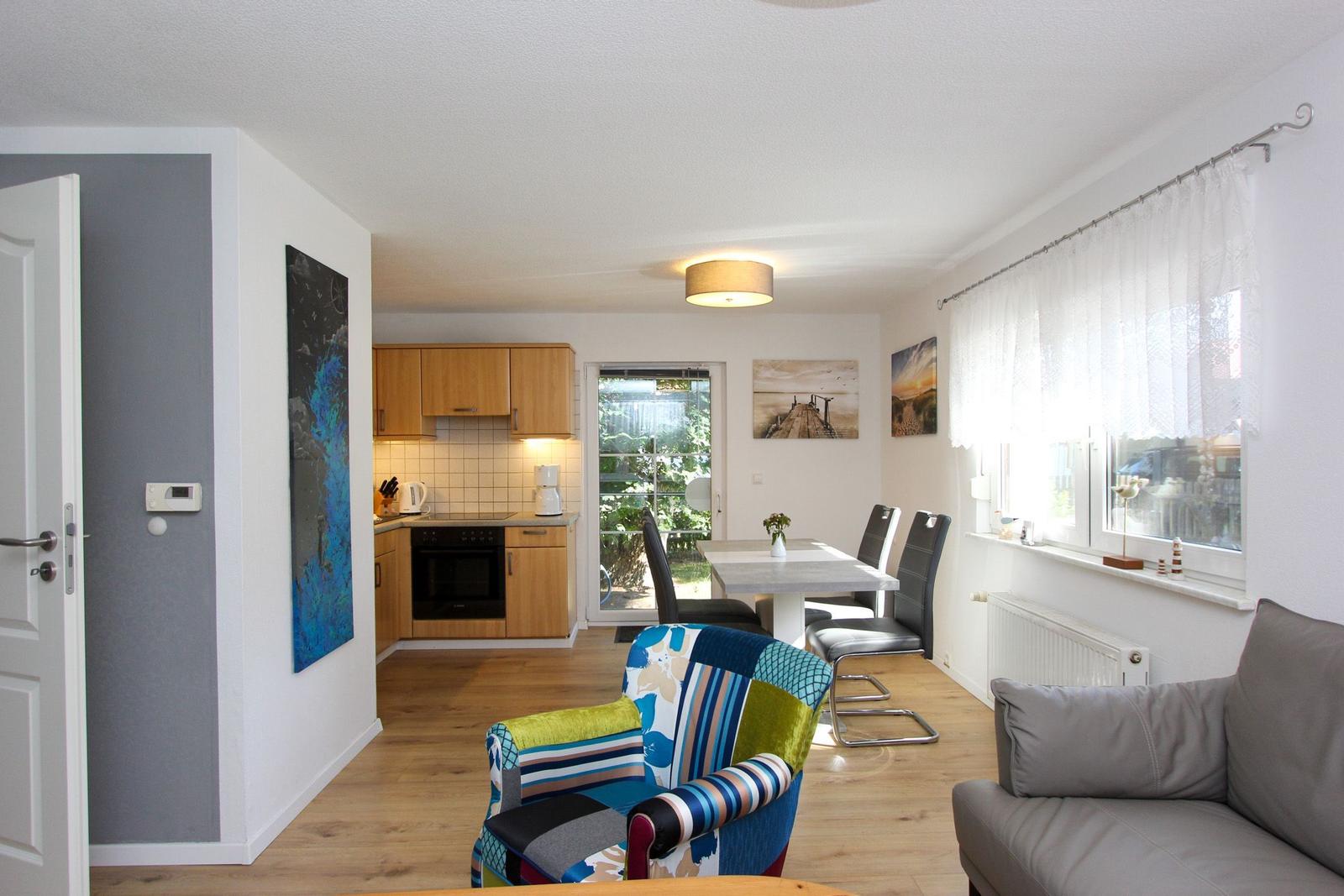 Wohnung mit Küche, Essbereich und Wohnzimmer. Holzboden, Fenster mit Vorhängen.
