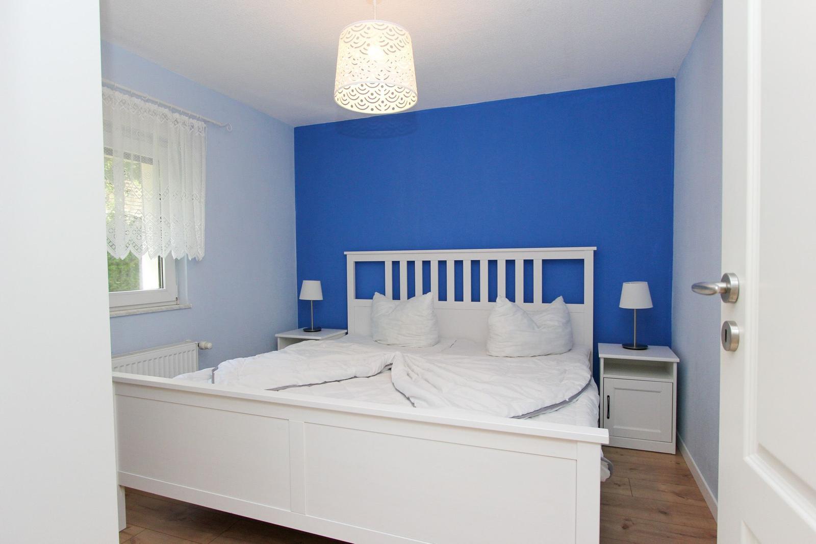 Schlafzimmer mit weißem Bett, blauer Wand und Nachttischen mit Lampen.