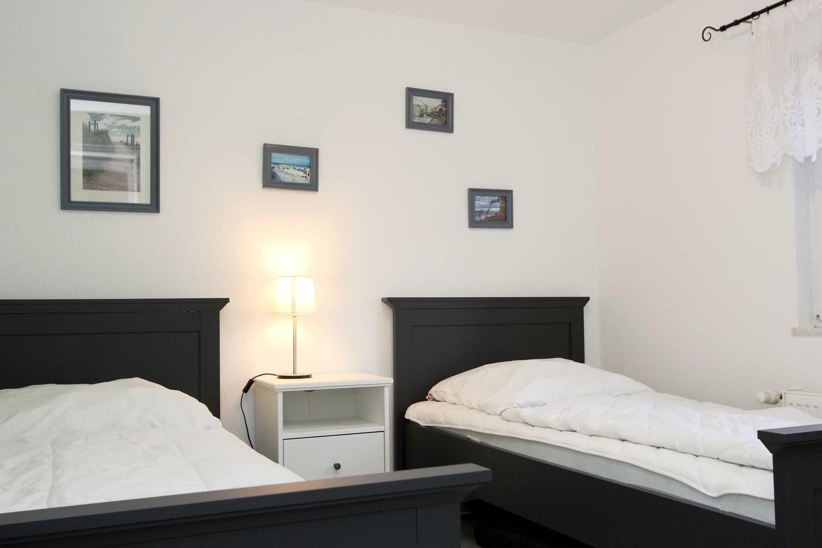 Zwei Einzelbetten mit weißen Bettwäschen, Nachttisch mit Lampe und Wandbilder.