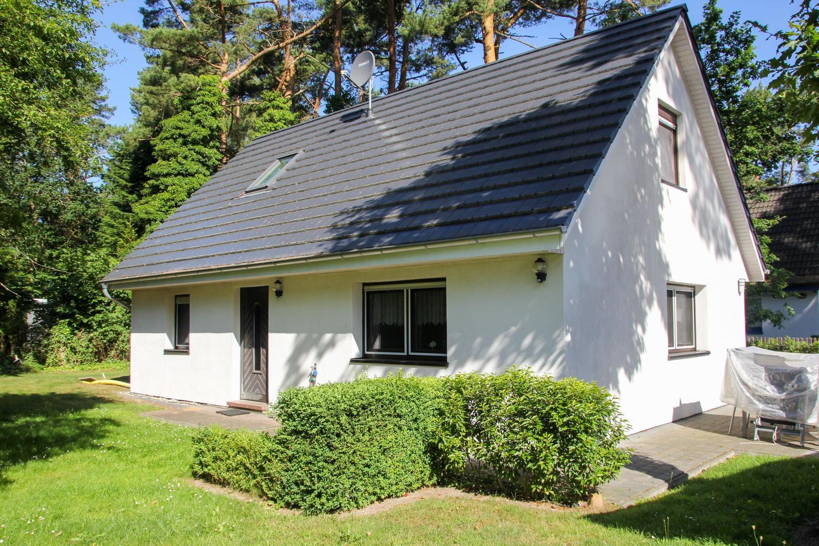 Ein weißes Haus mit dunklem Dach, umgeben von Gras und Bäumen.
