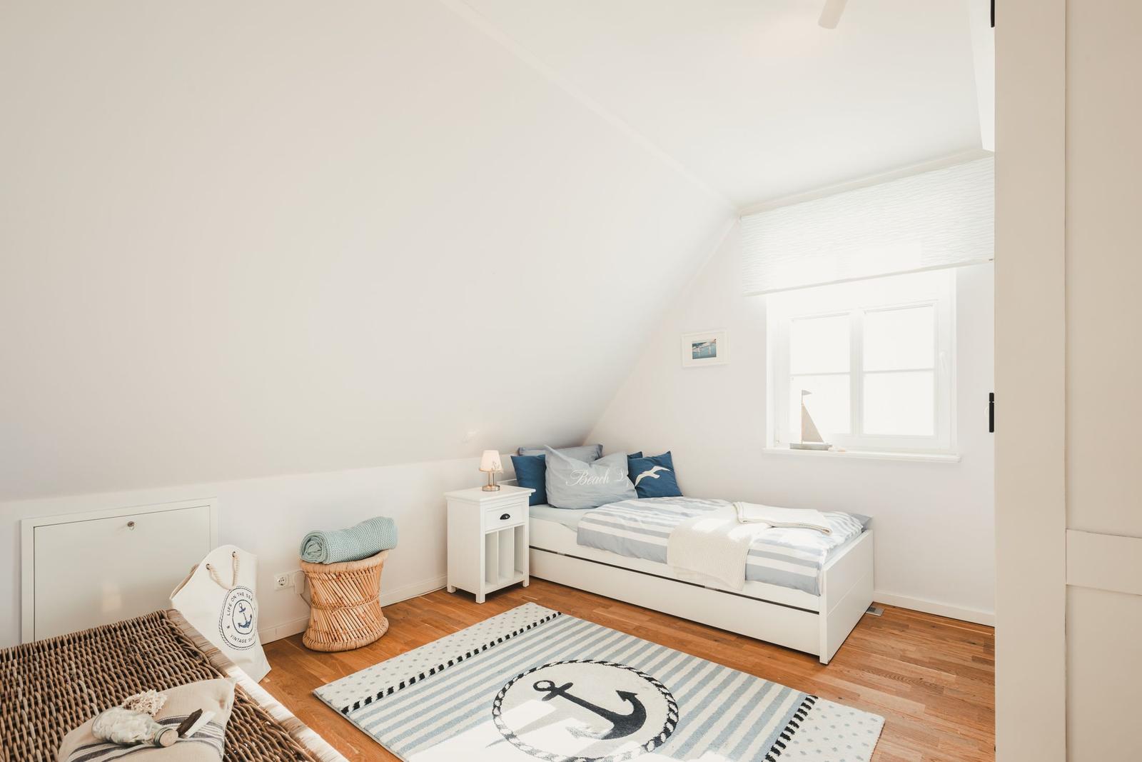 Schlafzimmer mit Dachschrägen, Bett, Nachttisch, Fenster und Teppich mit Ankergestaltung.