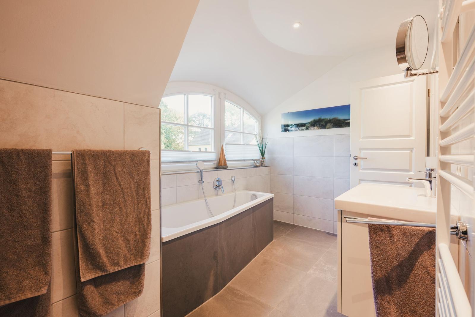 Badezimmer mit Badewanne, Fenster, Spiegel und Handtuchhalter.