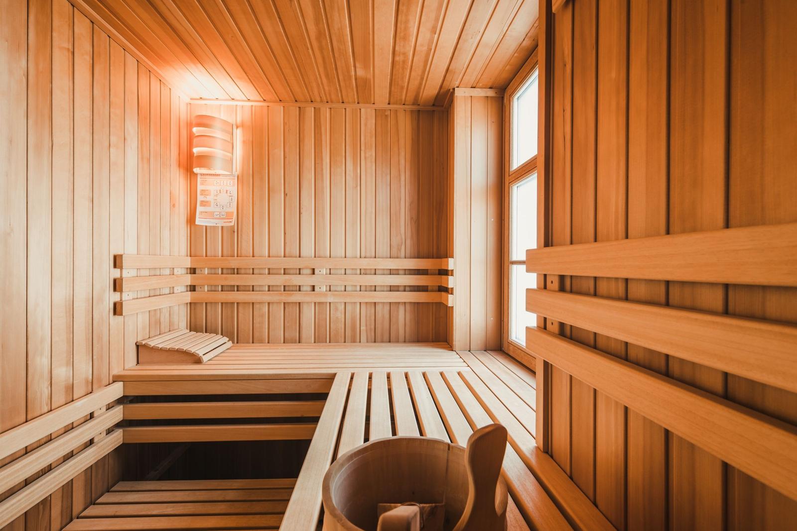 Holzsauna mit Sitzbänken und Fenster. Holzmulde und Wandlampe sichtbar.