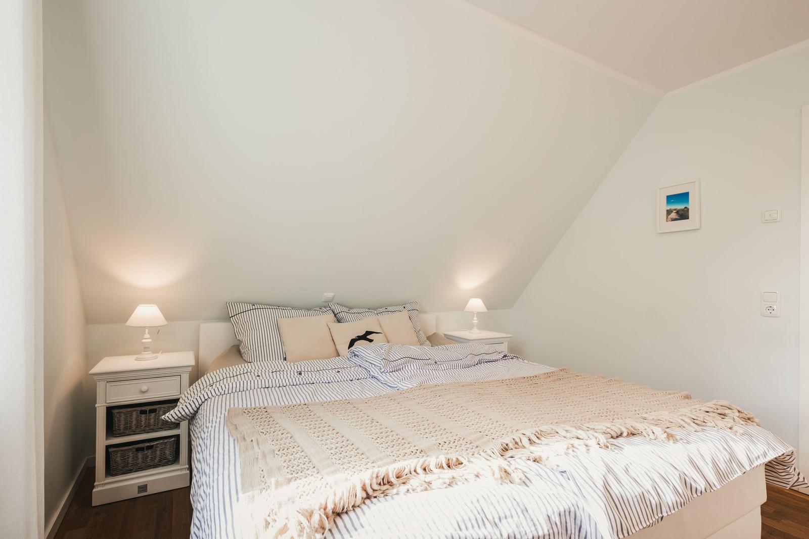Schlafzimmer mit Dachschrägen, Bett mit Streifenbezug und zwei Nachttischen mit Lampen.