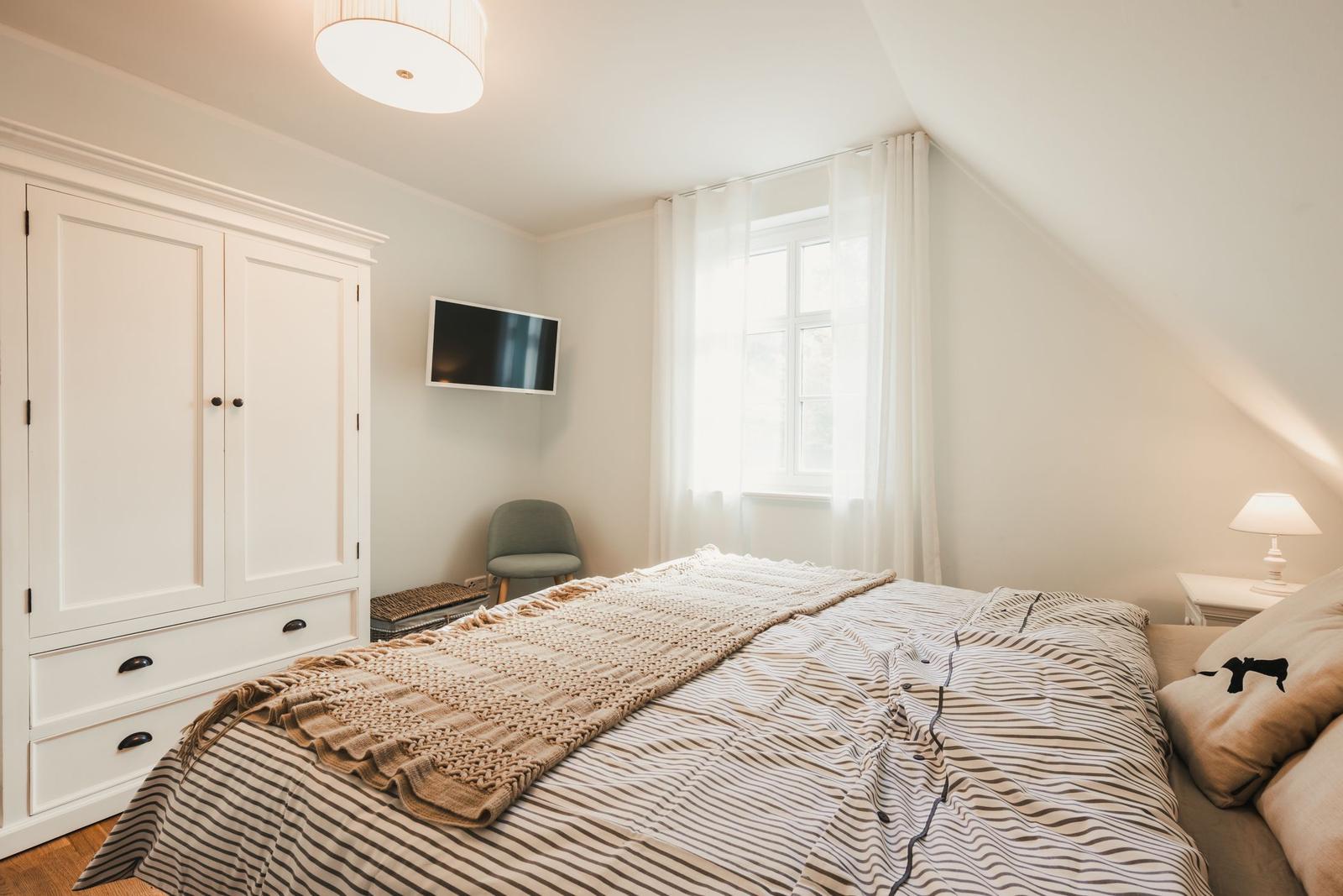 Schlafzimmer mit Bett, Kleiderschrank, Fenster und Fernseher an der Wand.