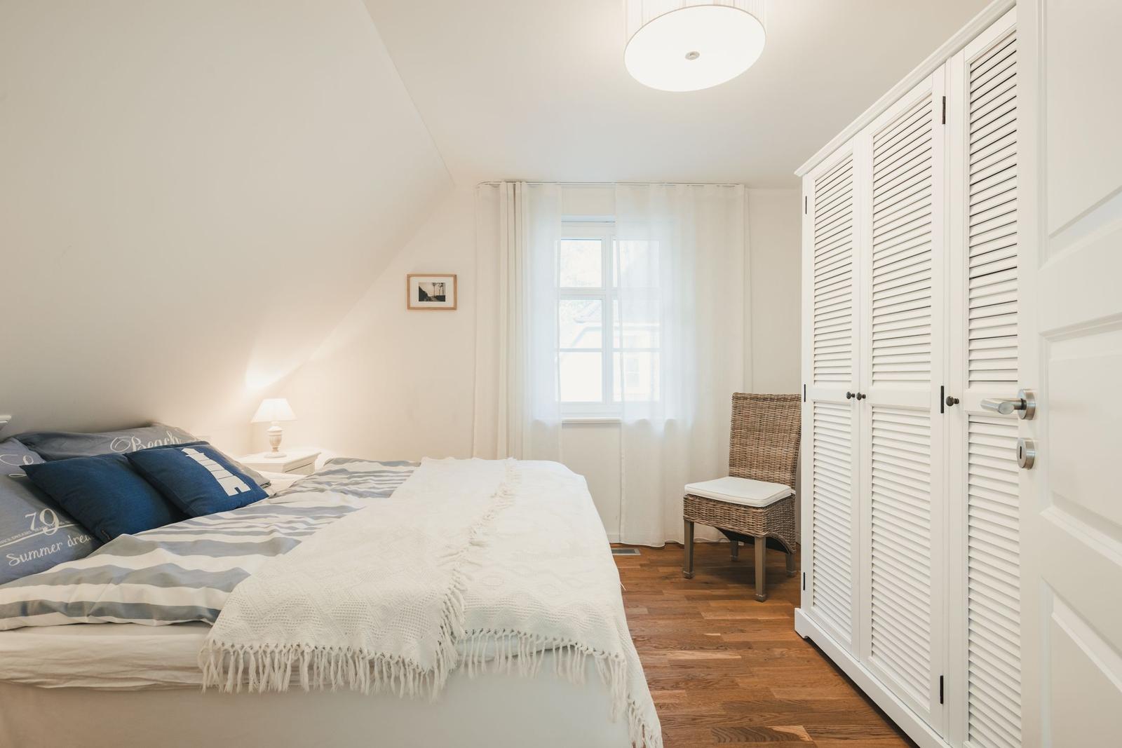 Schlafzimmer mit Bett, Kleiderschrank und Fenster mit Vorhängen.