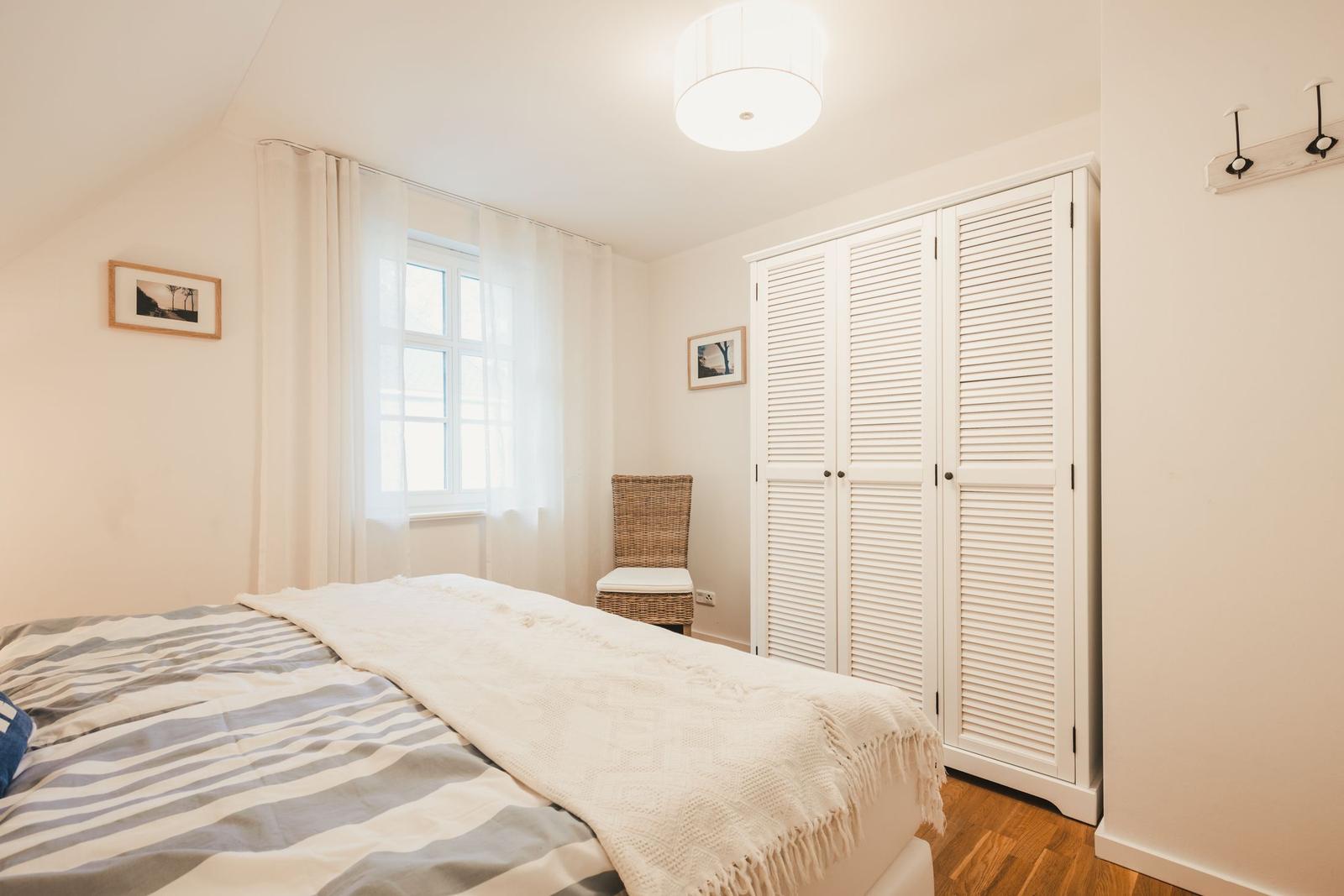 Schlafzimmer mit Bett, Kleiderschrank und Fenster mit Vorhängen.