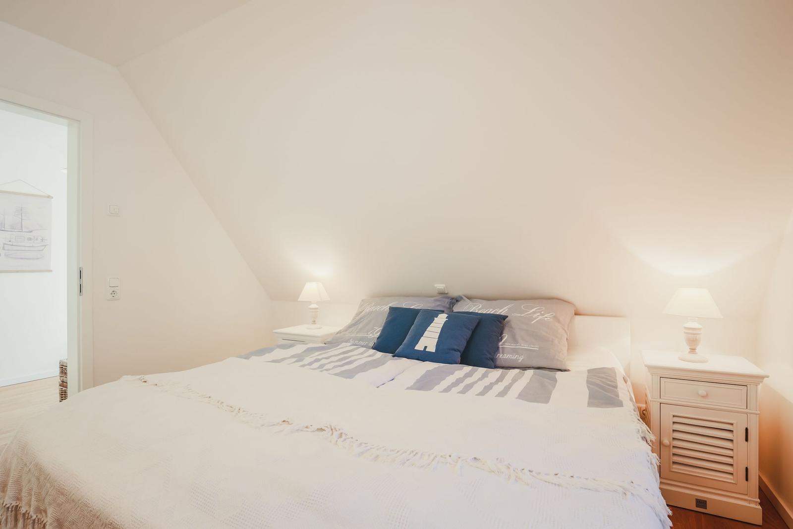 Schlafzimmer mit Bett, zwei Nachttischen und Lampen unter schrägen Wänden.