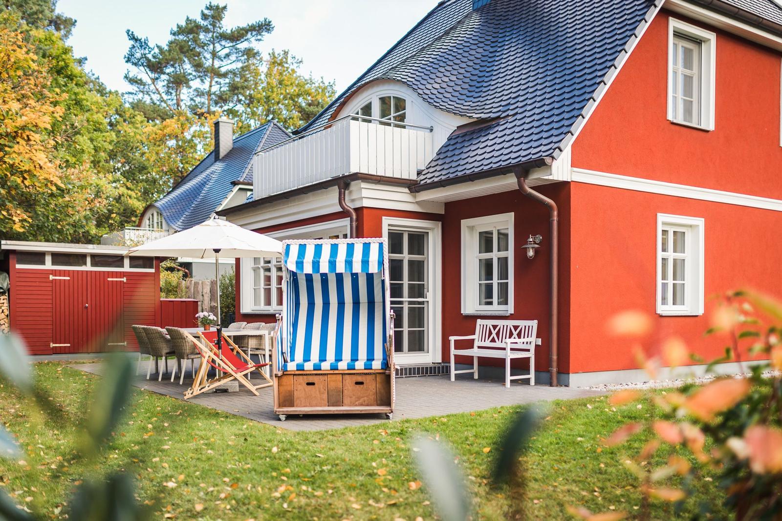 Rotes Haus mit Balkon, Terrasse und Strandkorb im Garten.