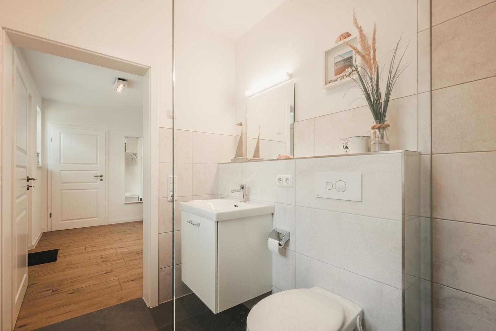 Badezimmer mit Waschbecken, Toilette und Dusche. Holzfußboden im Flur.