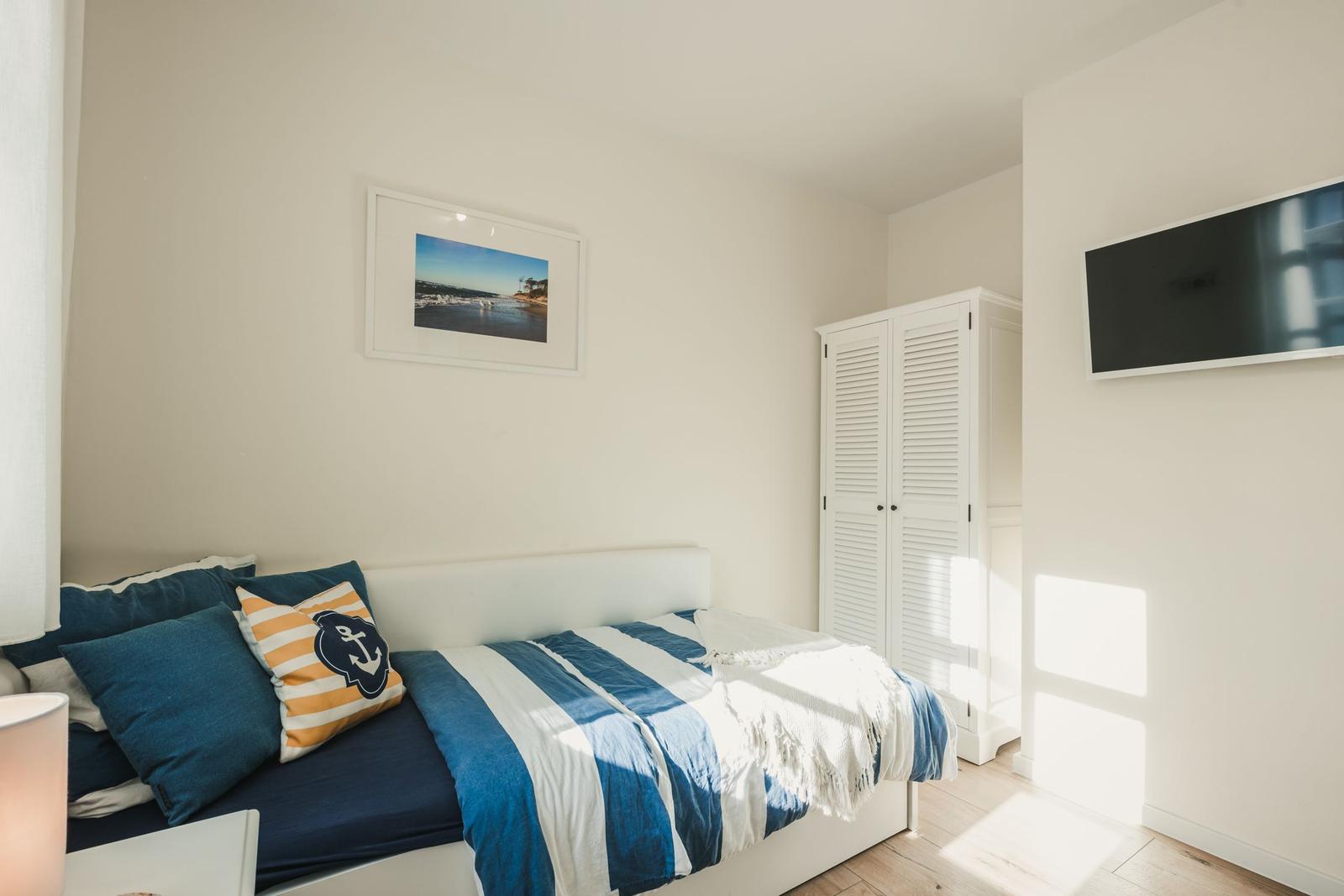 Schlafzimmer mit Bett, Kleiderschrank und Wandbild. TV an der Wand.