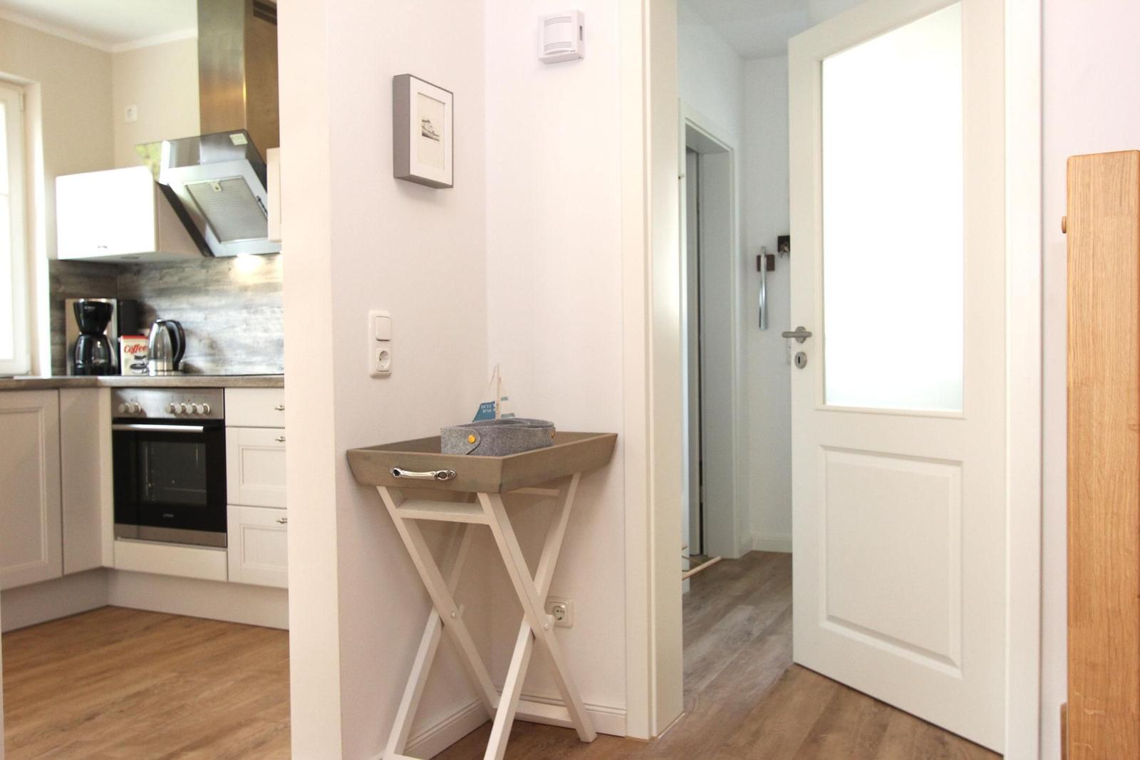 Küche mit Kochfeld und Backofen. Flur mit Tür und kleinem Tisch.
