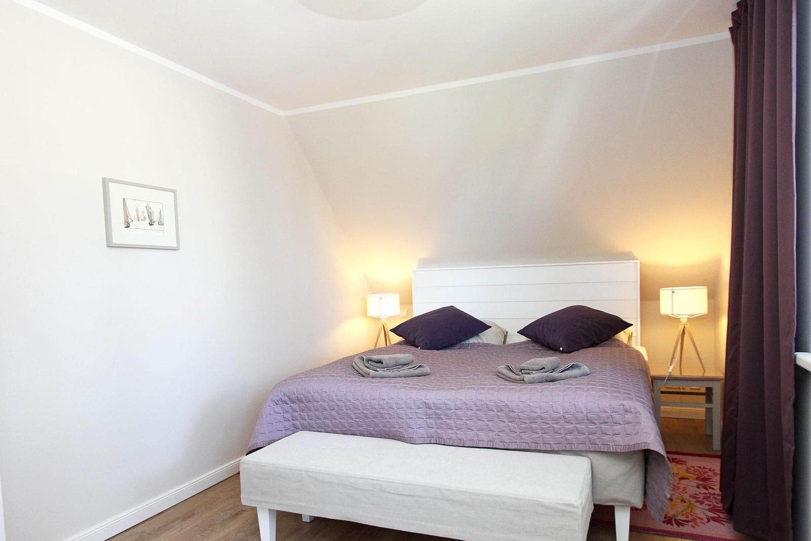 Schlafzimmer mit Bett, zwei Nachttischen und Lampen. An der Wand hängt ein Bild.