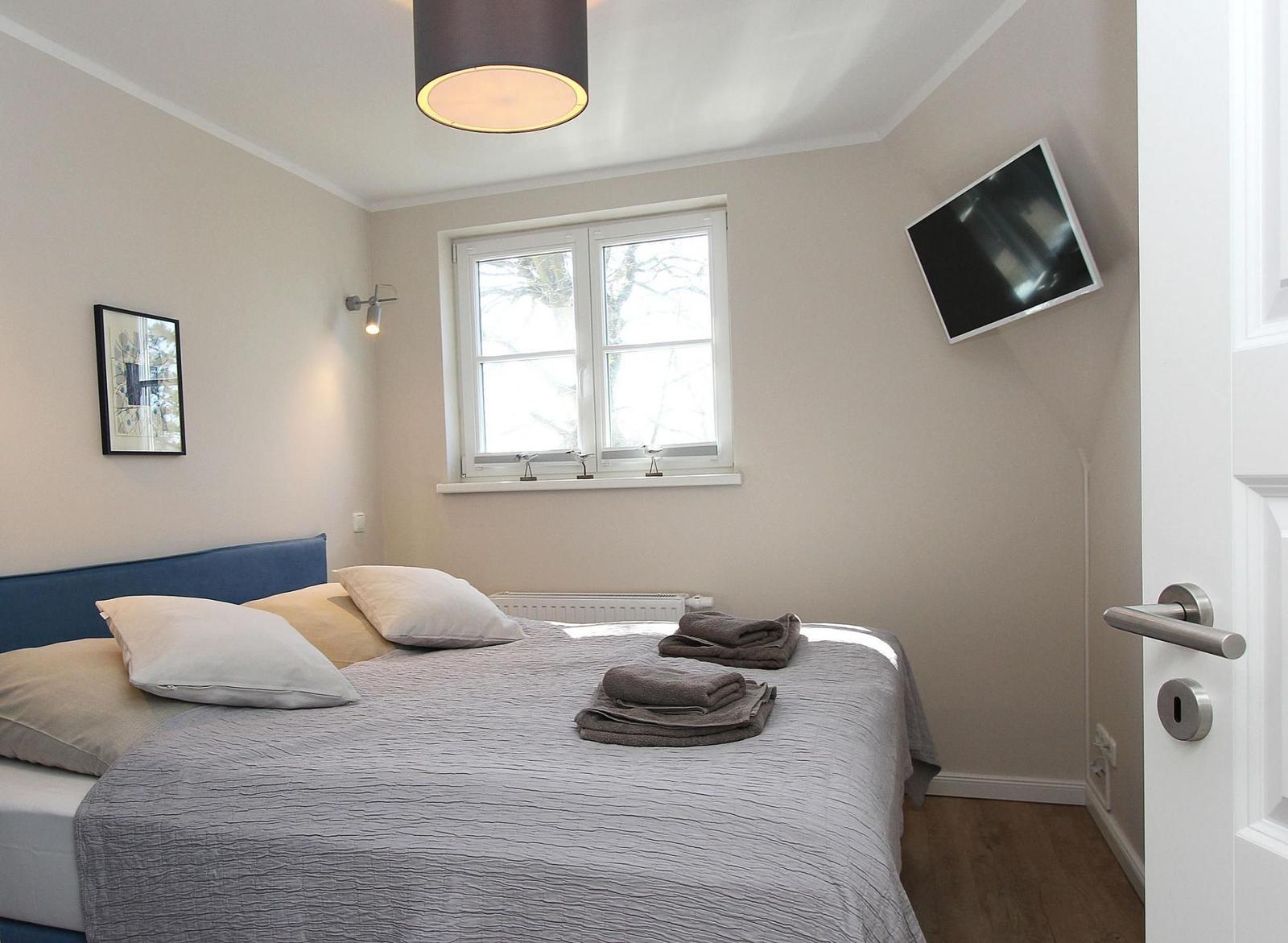 Schlafzimmer mit Bett, Fenster, TV und Deckenleuchte.