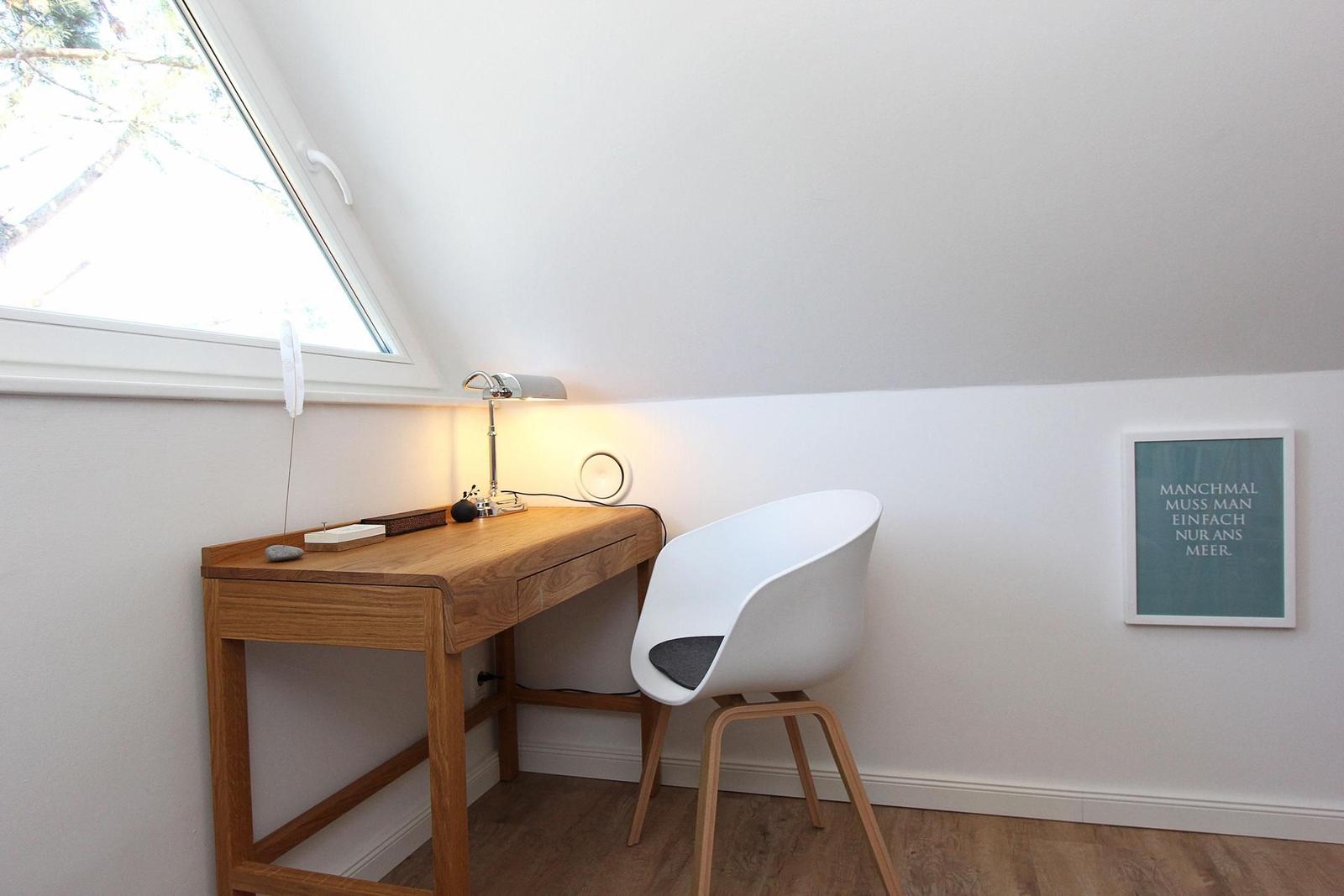 Schreibtisch mit Stuhl unter Dachfenster. Wandbild und Lampe sind sichtbar.