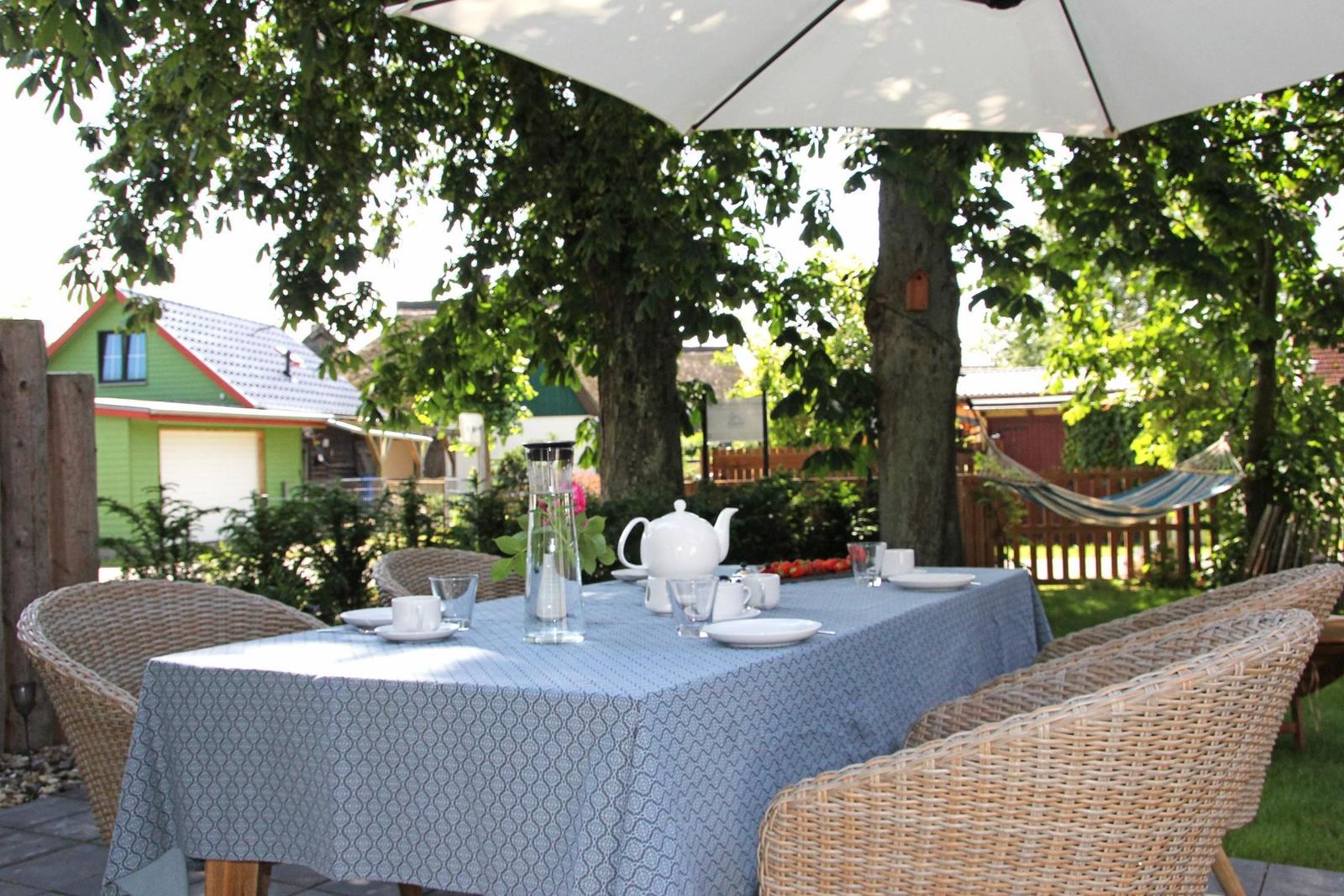 Garten mit gedecktem Tisch unter Sonnenschirm und Hängematte zwischen Bäumen.