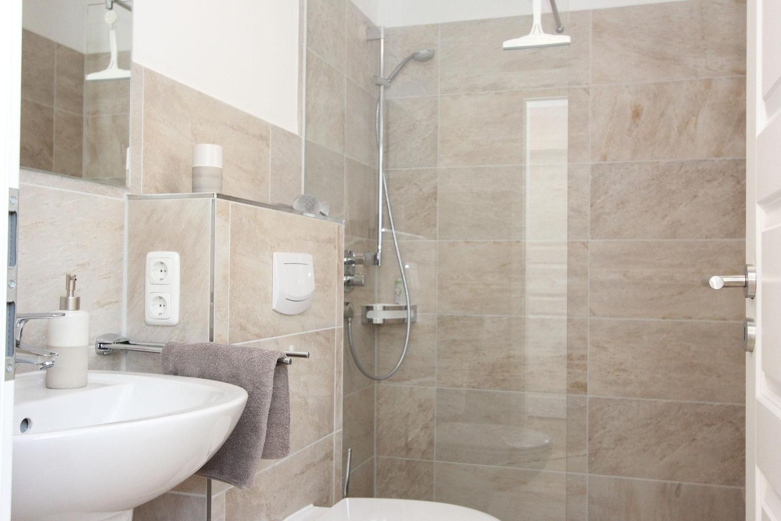 Badezimmer mit Dusche, Waschbecken und Toilette. Fliesen und Spiegel sind sichtbar.