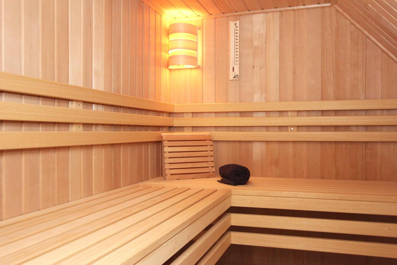 Sauna mit Holzbänken, Thermostaten und einer dunklen Decke.