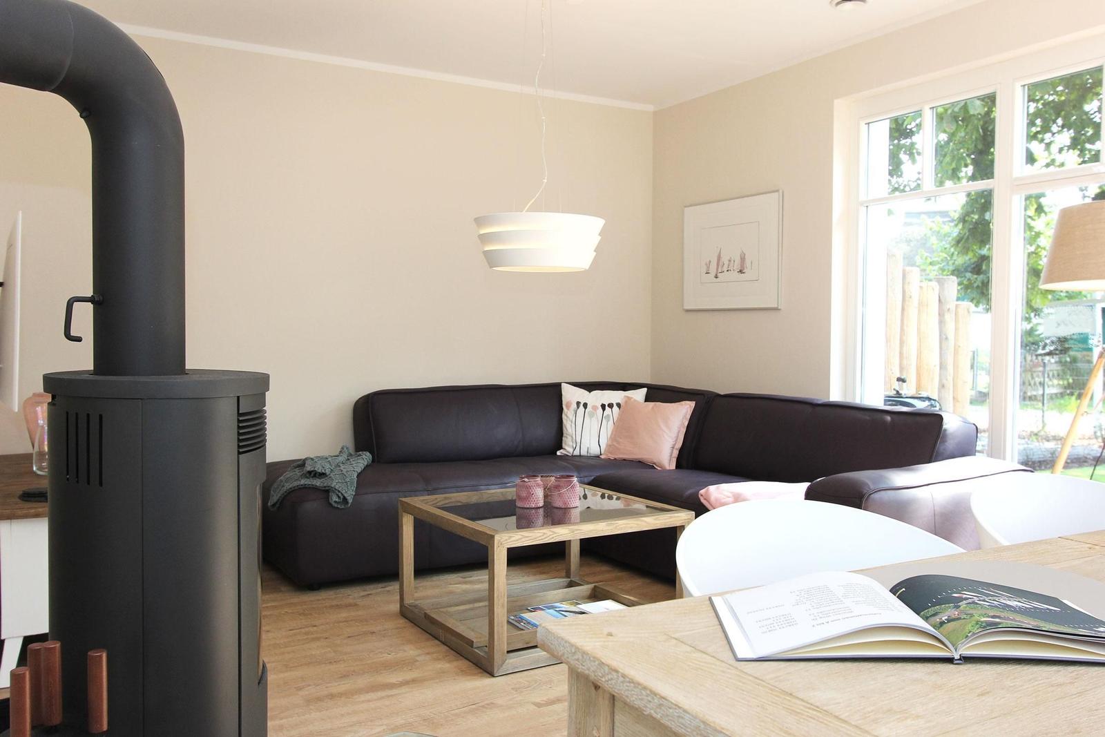 Wohnzimmer mit Sofa, Kamin und Glas-Tisch. Fenster mit Blick auf Garten.