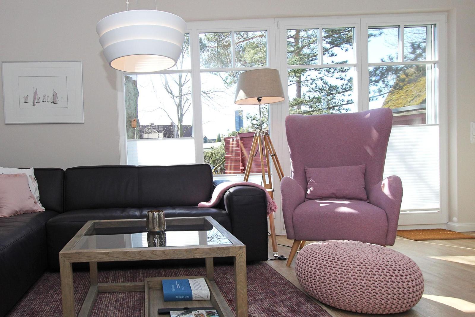 Wohnzimmer mit Sofa, Sessel und Tisch. Fenster mit Blick auf Bäume.