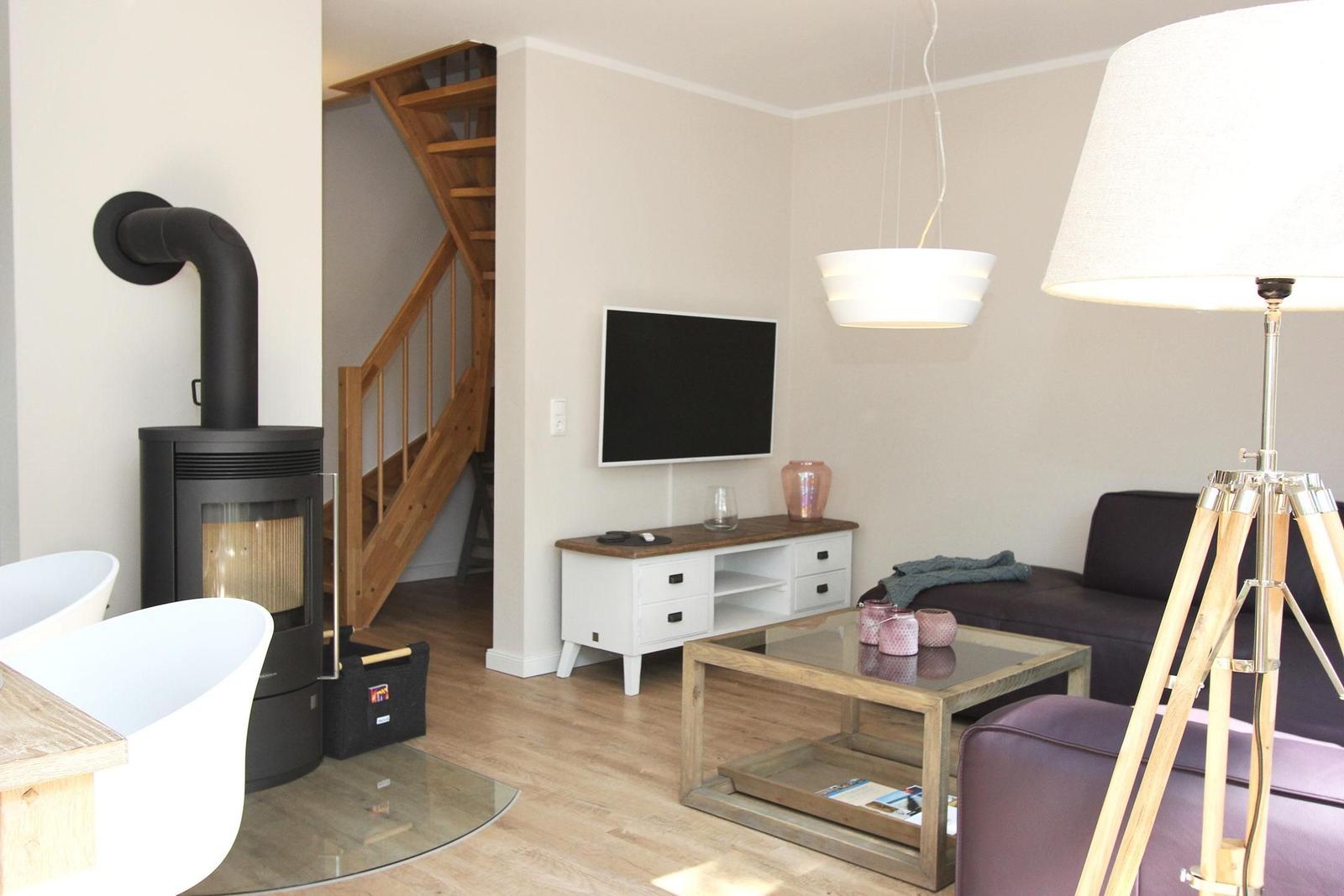 Wohnzimmer mit Kamin, TV, Sofa und Stehlampe. Holztreppe führt zur oberen Etage.