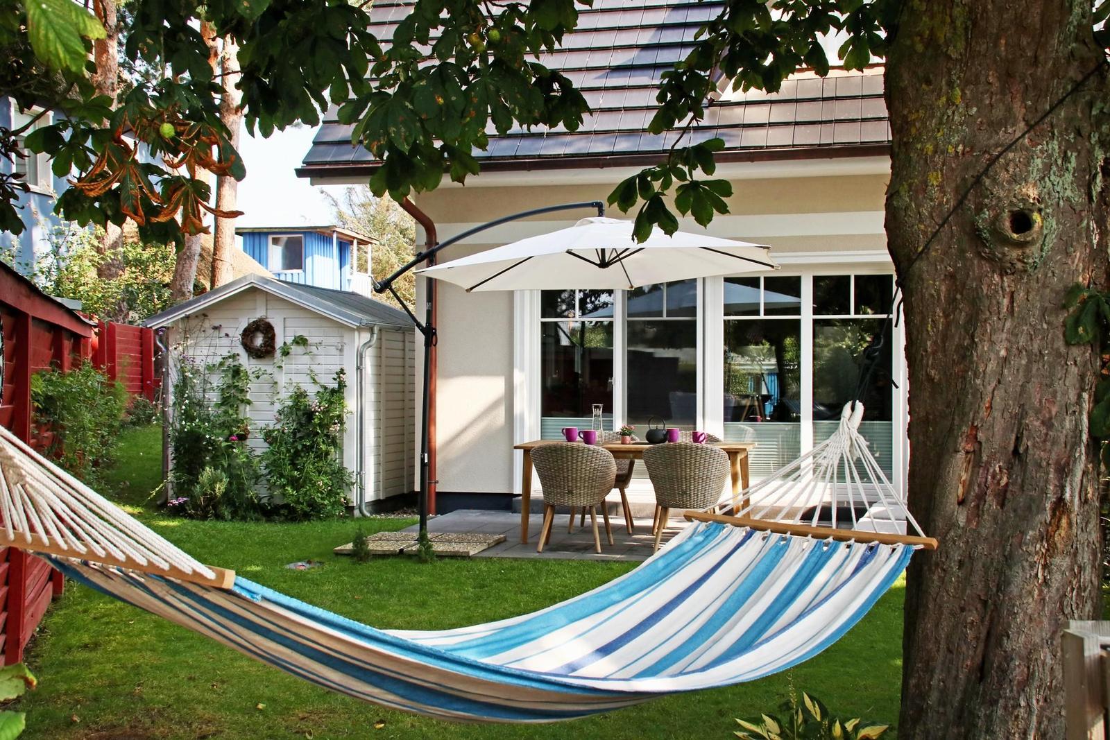 Hängemattensitzplatz zwischen Baum und Terrasse mit Tisch und Stühlen unter Sonnenschutz.