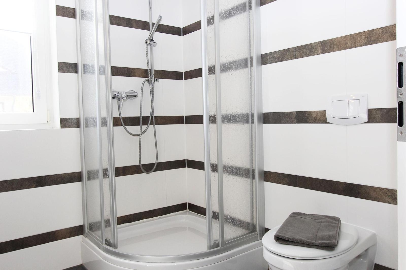 Badezimmer mit Dusche, Toilette und Fenster. Wände mit weißen und braunen Streifen.