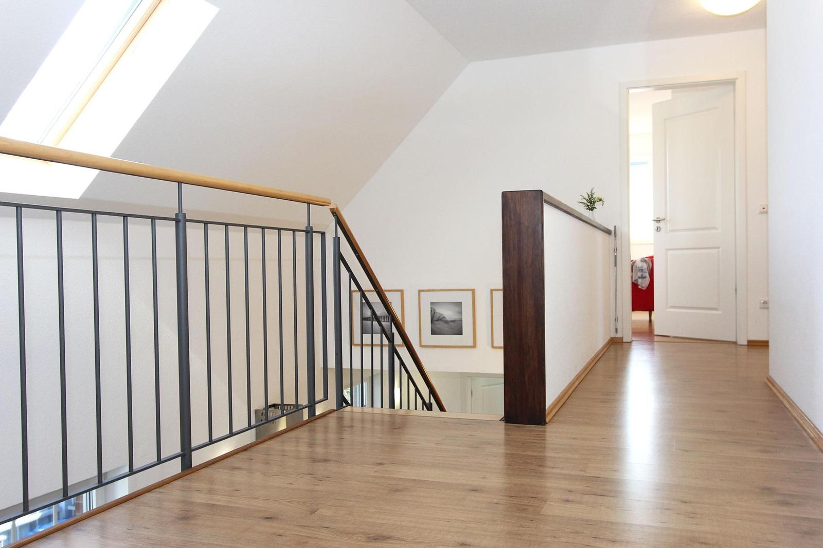 Haus mit Holzboden, Treppe und Dachfenster. Weiße Wände und Bilderrahmen.