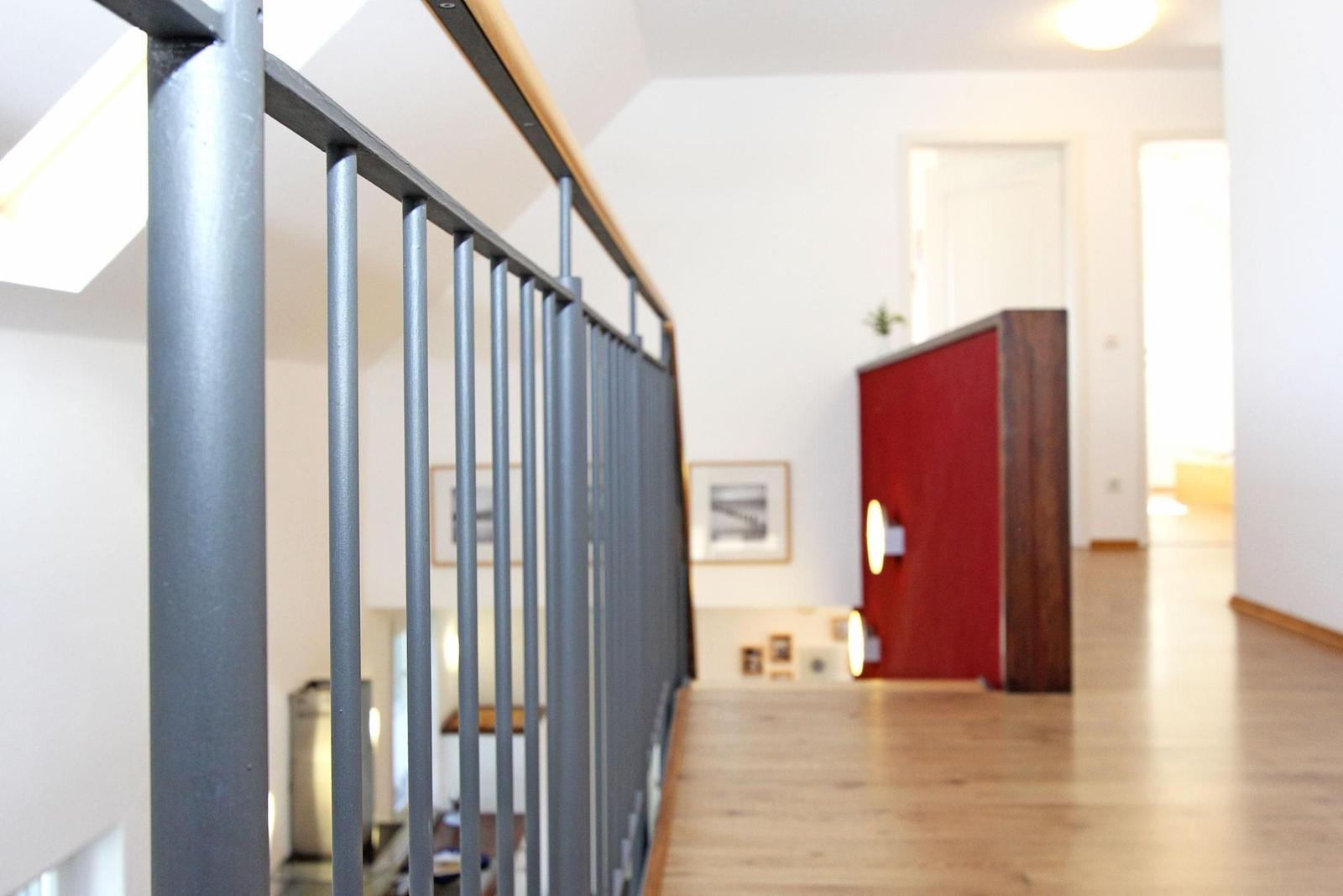 Treppenhaus mit grauem Geländer und rotem Schrank im Hintergrund.