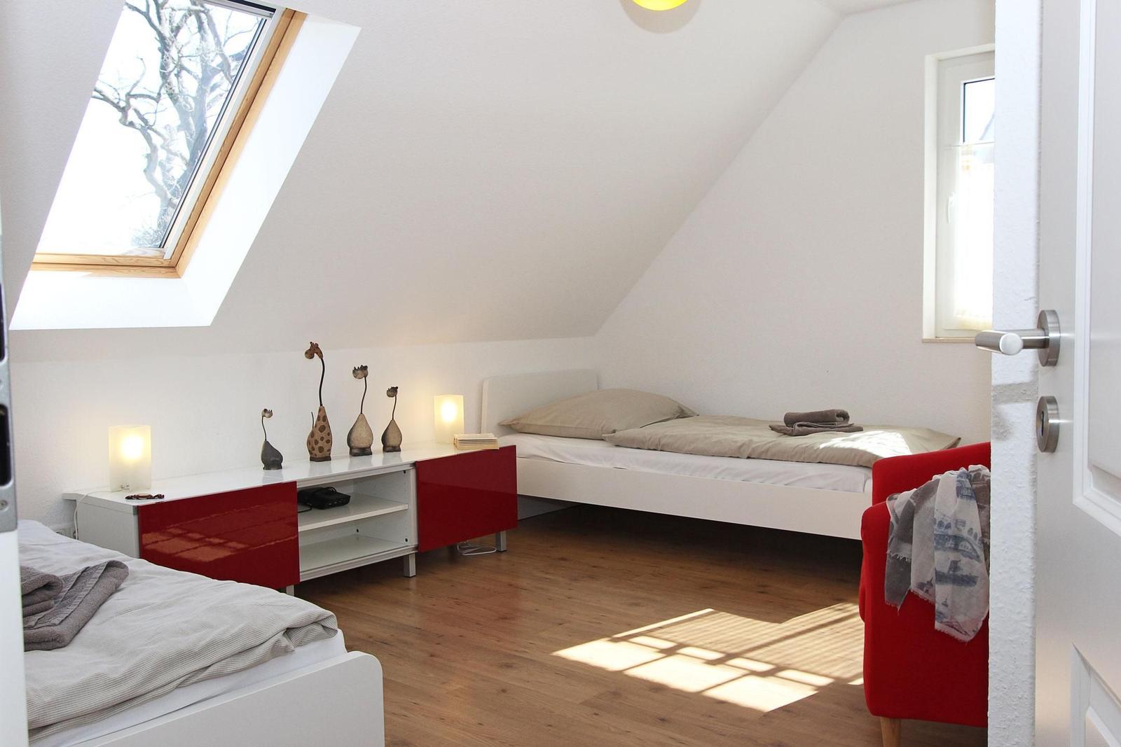 Zimmer mit Dachschrägen, zwei Betten, rotem Schrank und Fenster.