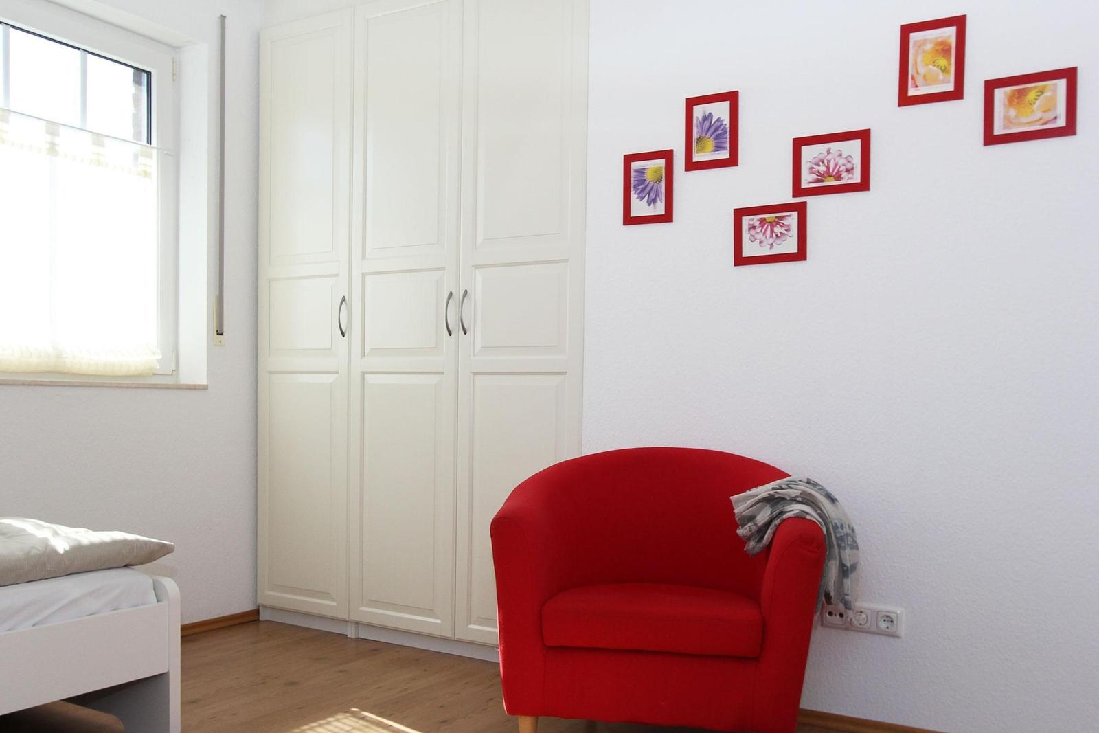 Ein Raum mit weißem Schrank, rotem Sessel und Bildern an der Wand.