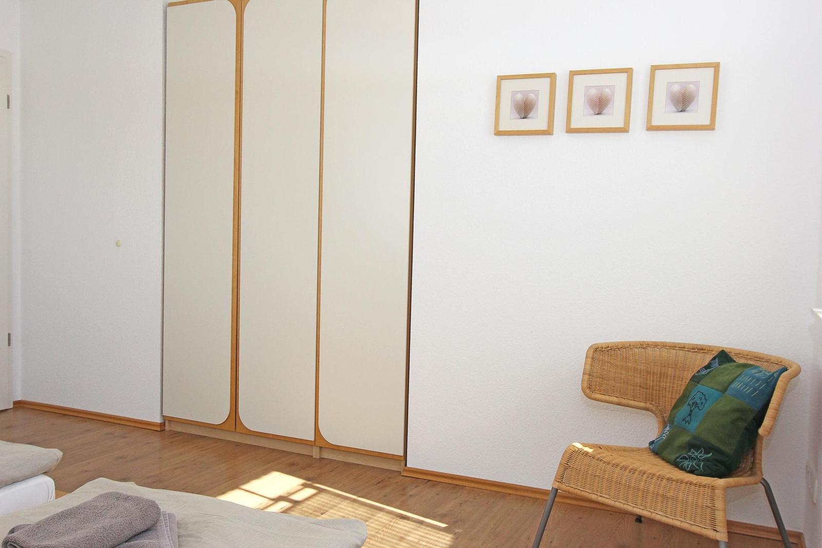 Schlafzimmer mit Kleiderschrank, Stuhl und Wandbildern.