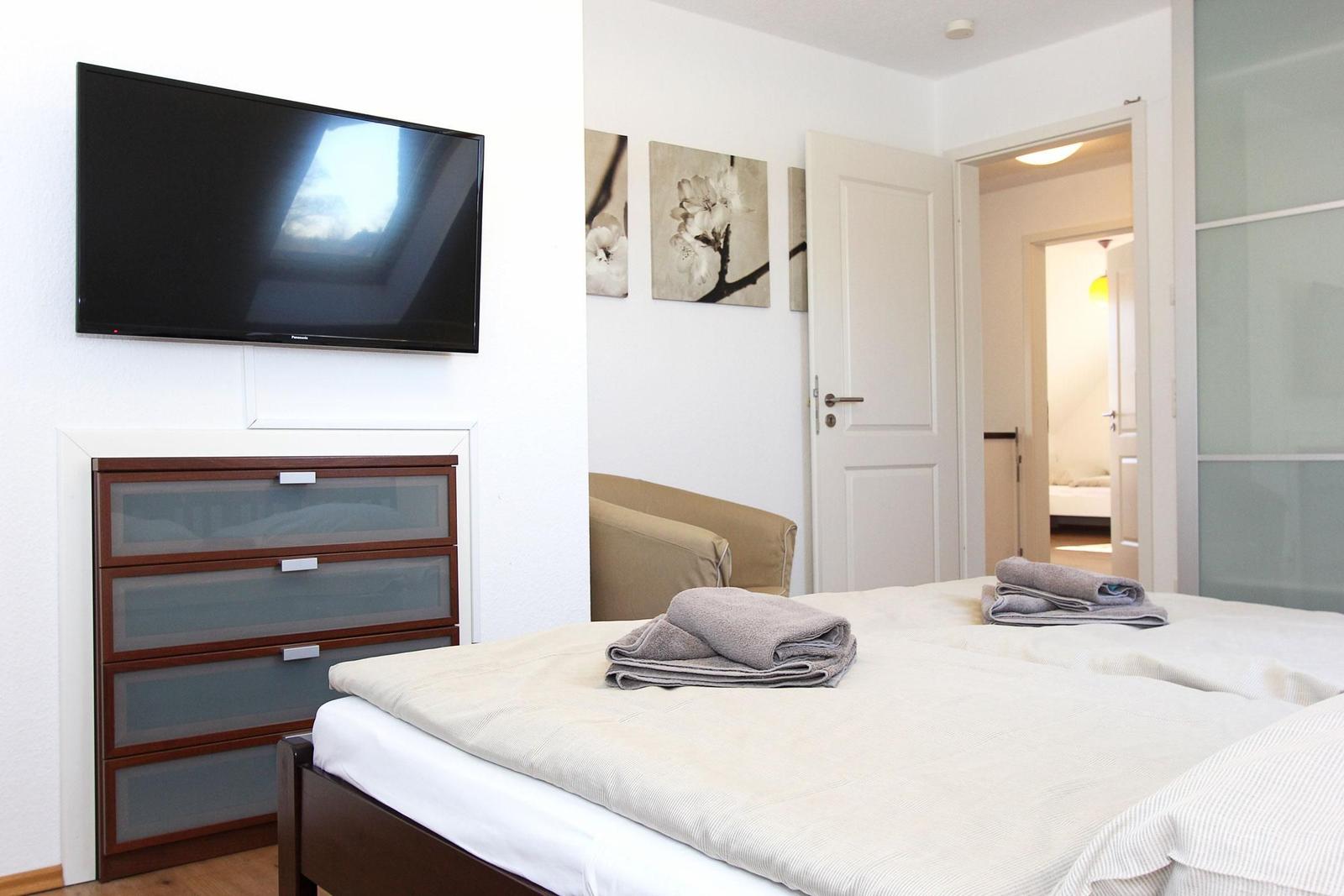 Schlafzimmer mit Bett, Fernseher und Schrank. Türen führen in angrenzende Räume.
