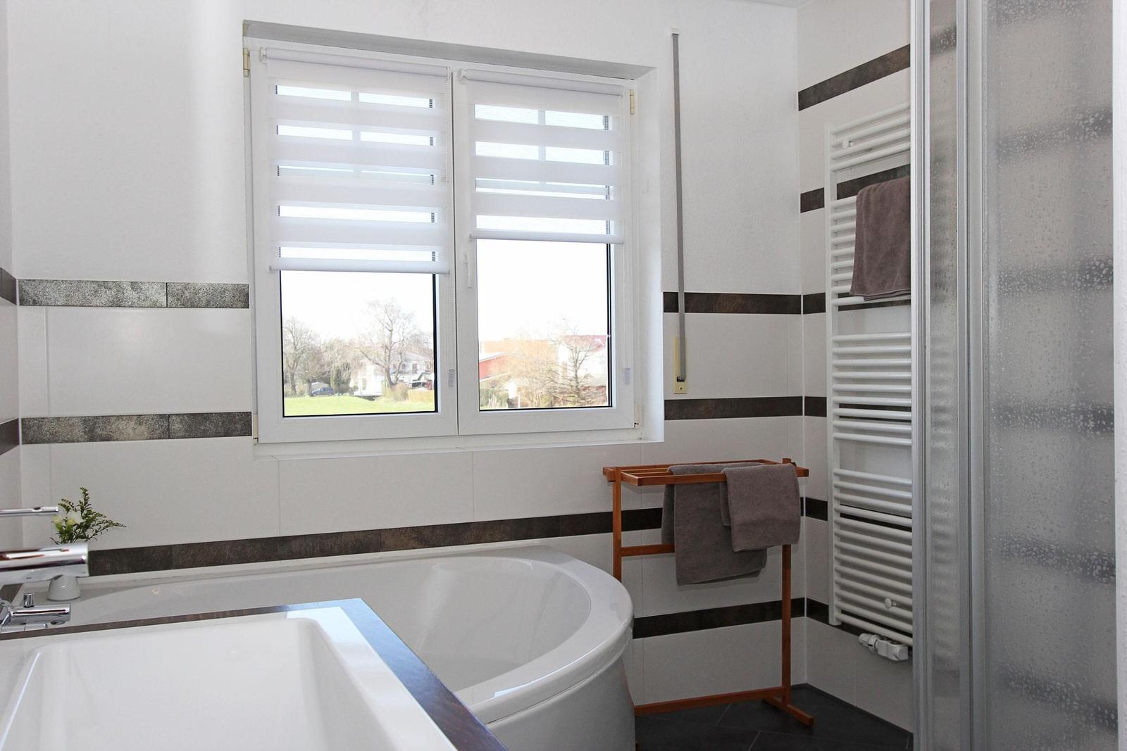 Badezimmer mit Badewanne, Dusche und Fenster mit Jalousie.
